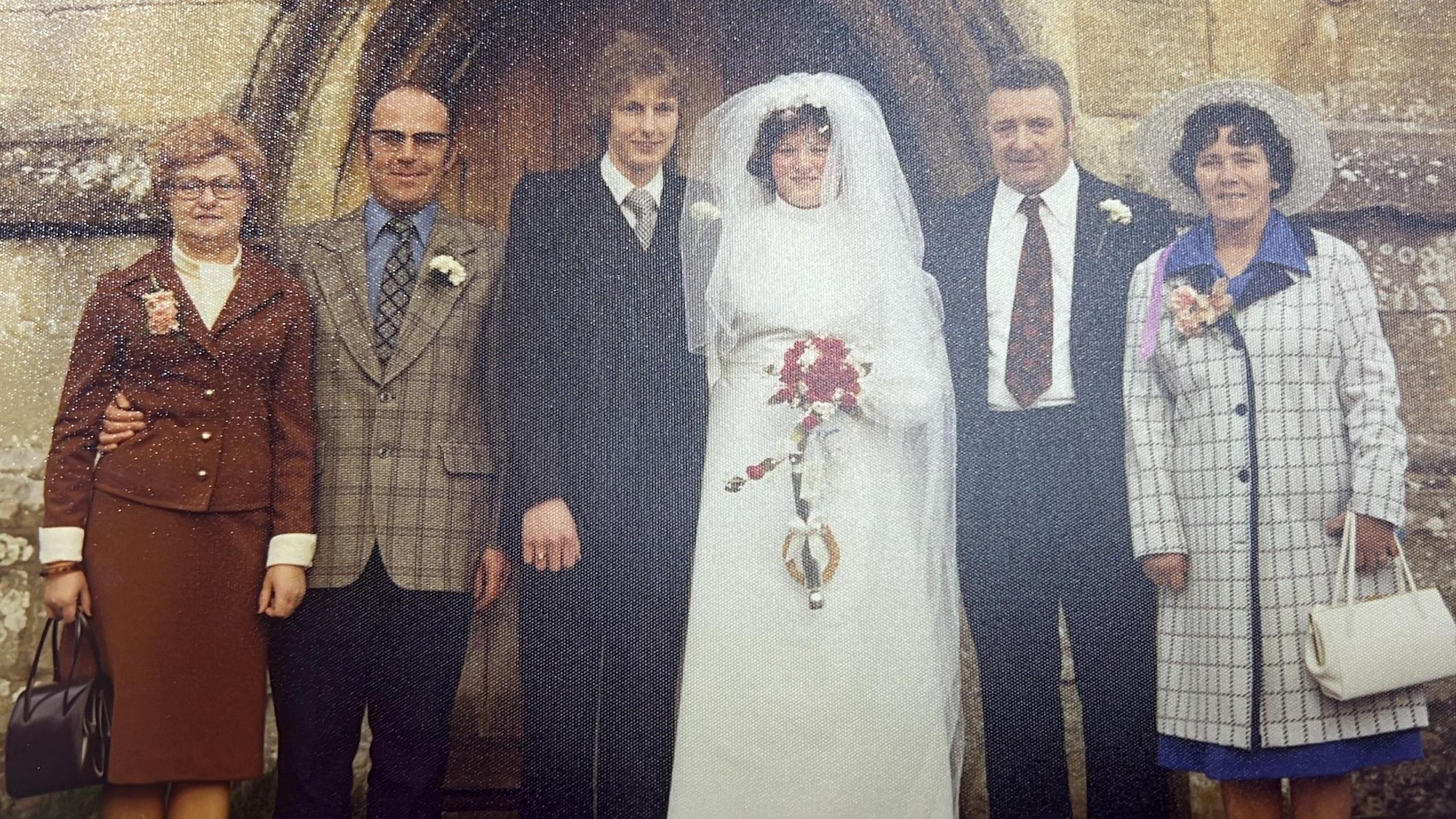 An old wedding photo outside a church door: a group, with bride and groom in the middle (Kevin and Jackie), and sets of people on either side of them, two men in smart suits and two women dressed smartly.