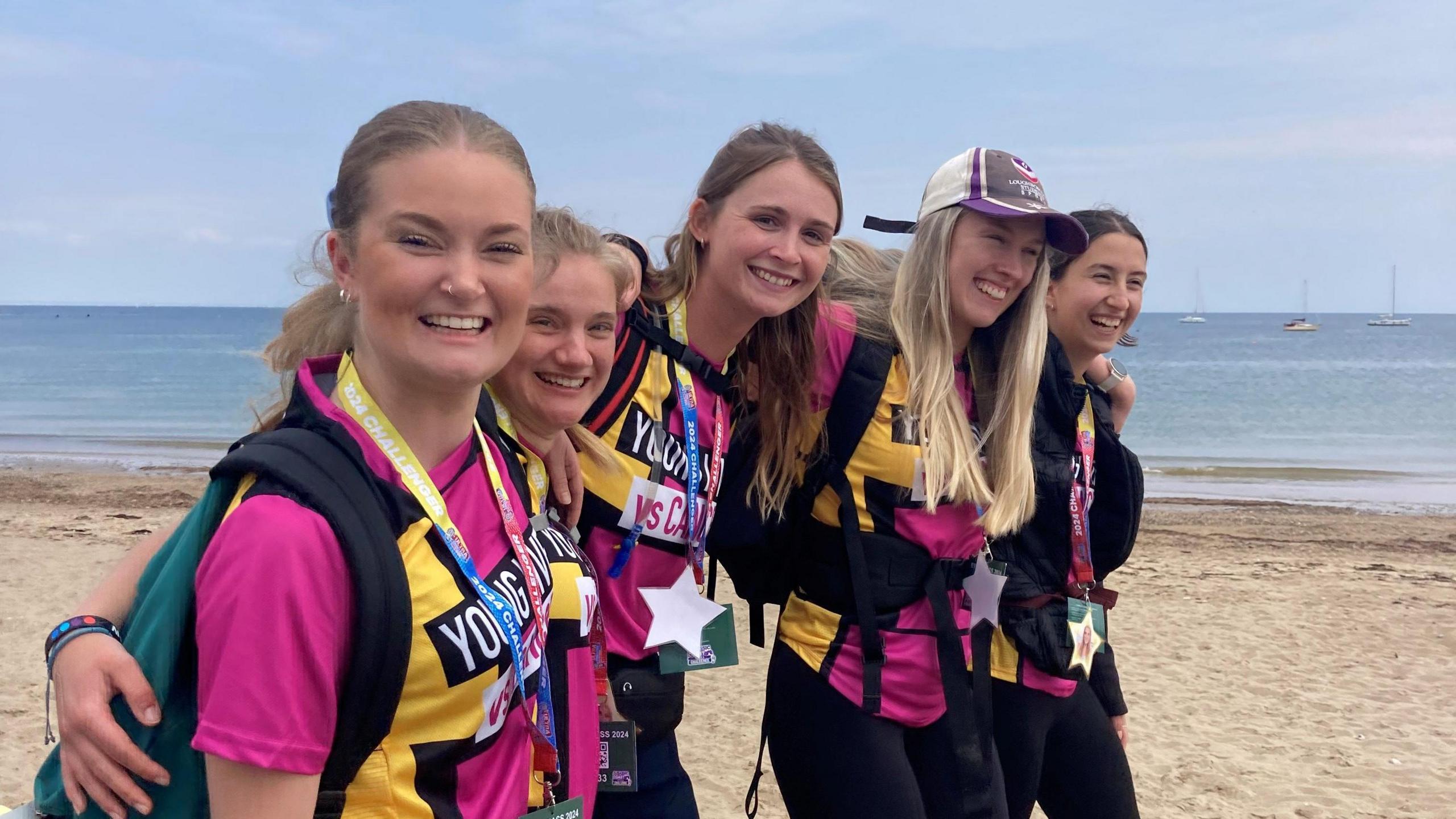 Five friends wearing pink t-shirt smiling at camera near sea