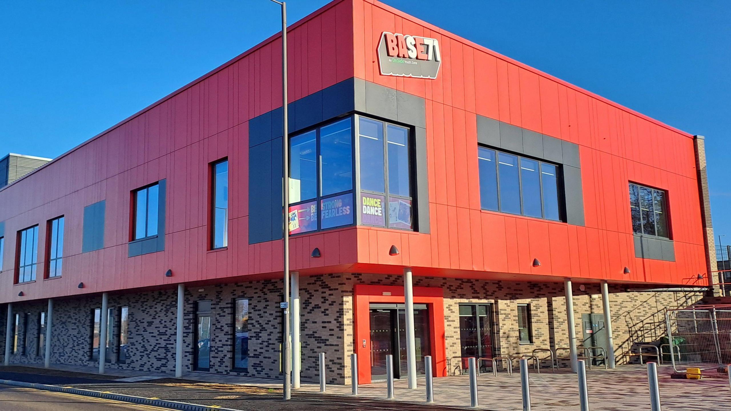 An exterior shot of the two-story building, which is cladded in bright red panels and has large windows.