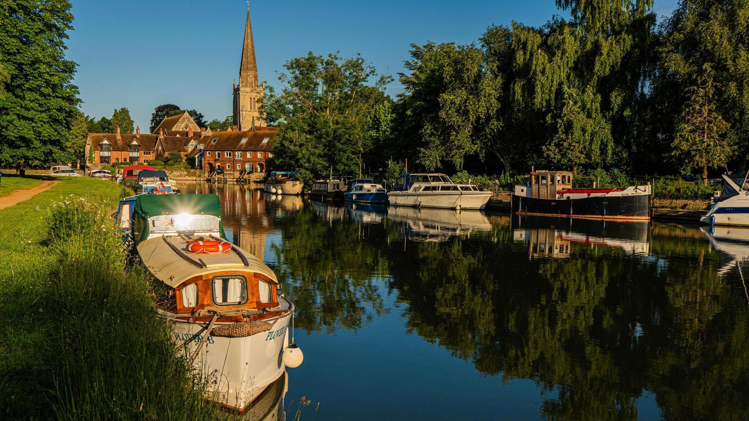 TUESDAY - Sunrise over a still river with perfect reflections of boats and a church spire against a blue sky