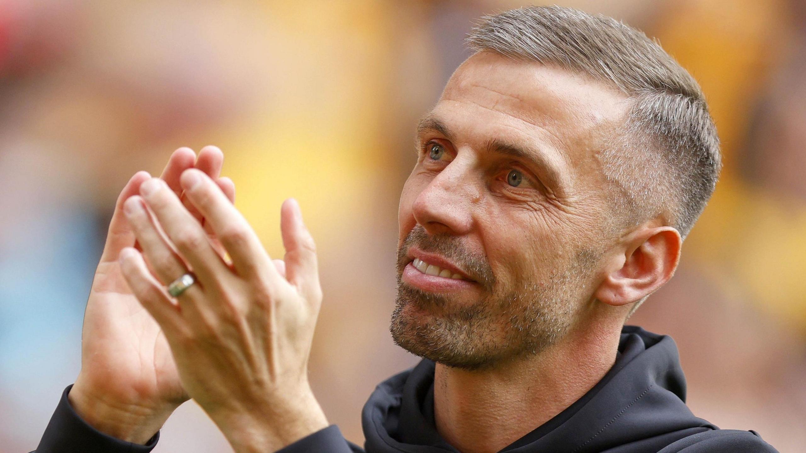 Gary O'Neil looks upwards with raised hands and applauds the fans while wearing a dark hoodie 