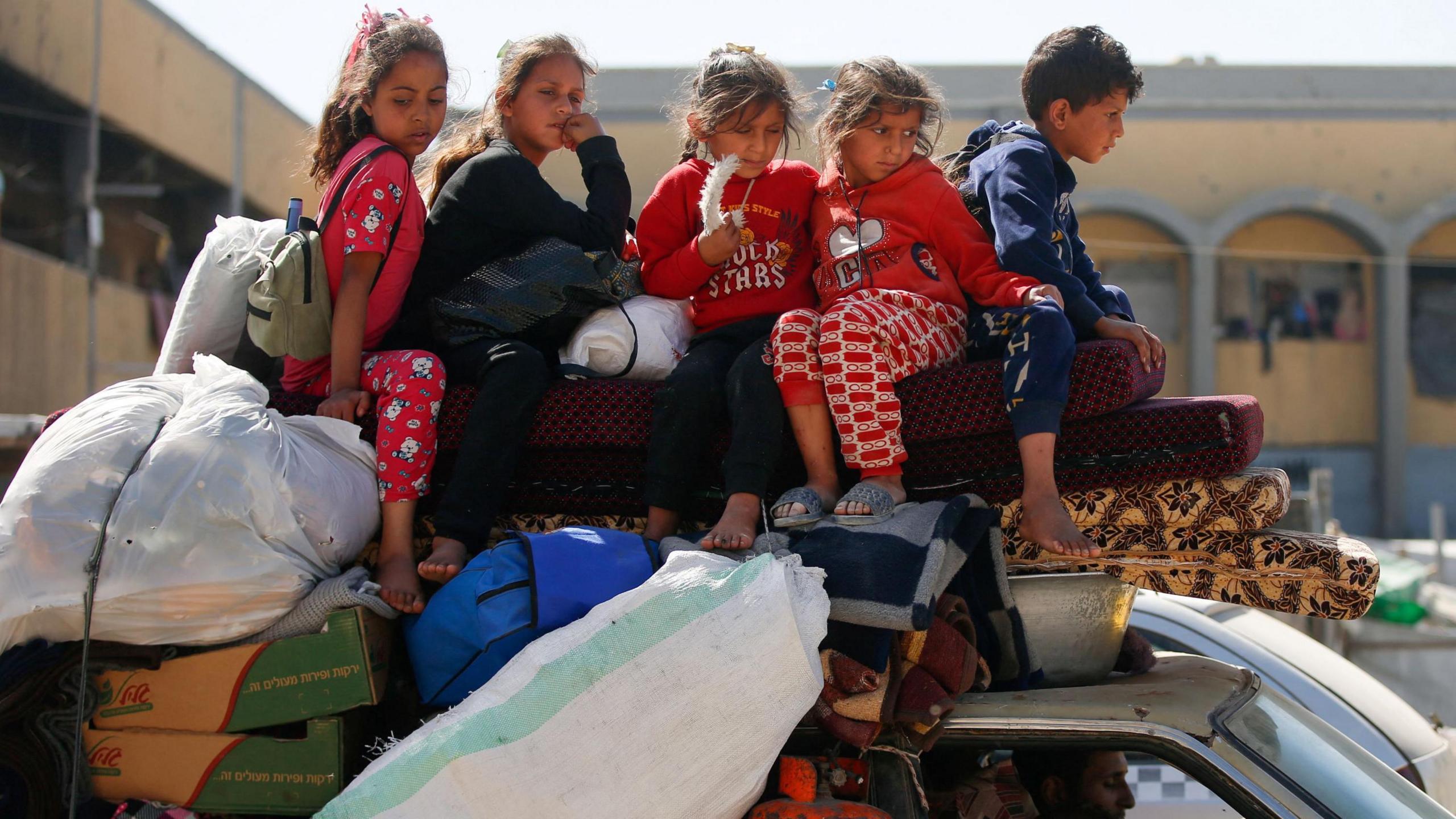 Five children sit atop luggage piled on a car