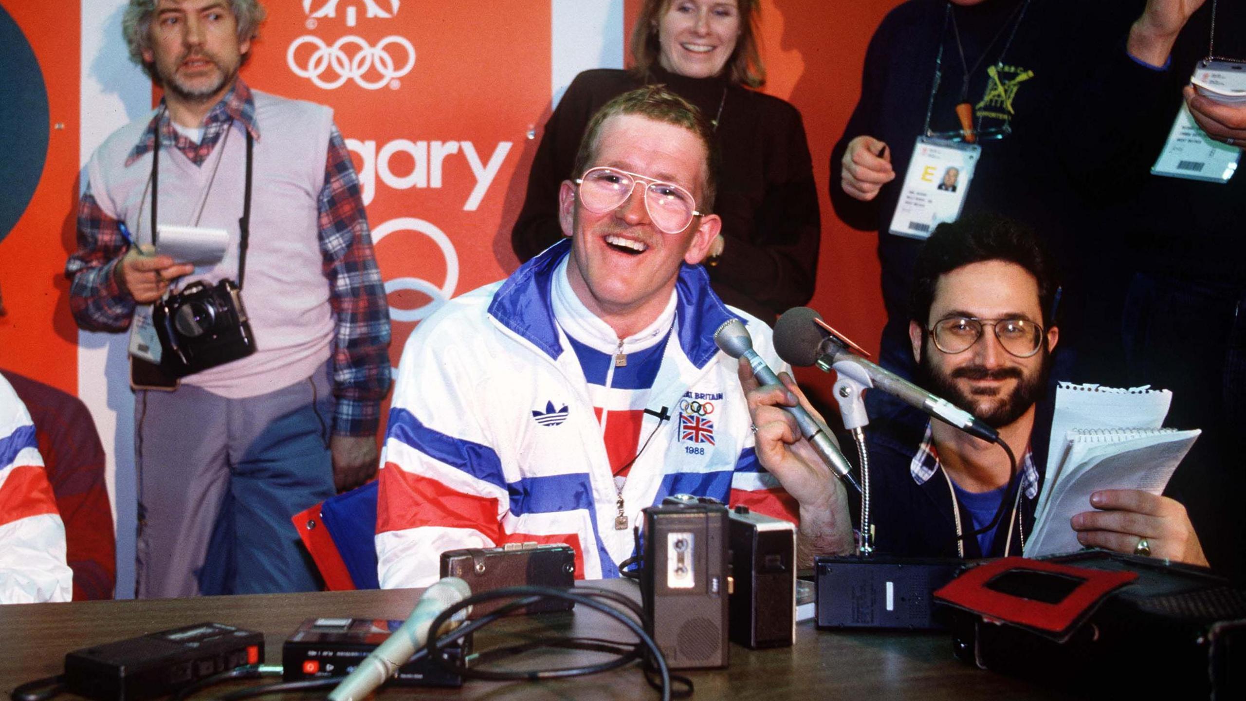 Eddie Edwards wearing a red, white and blue GB kit, sitting at a table with a microphone and recorders