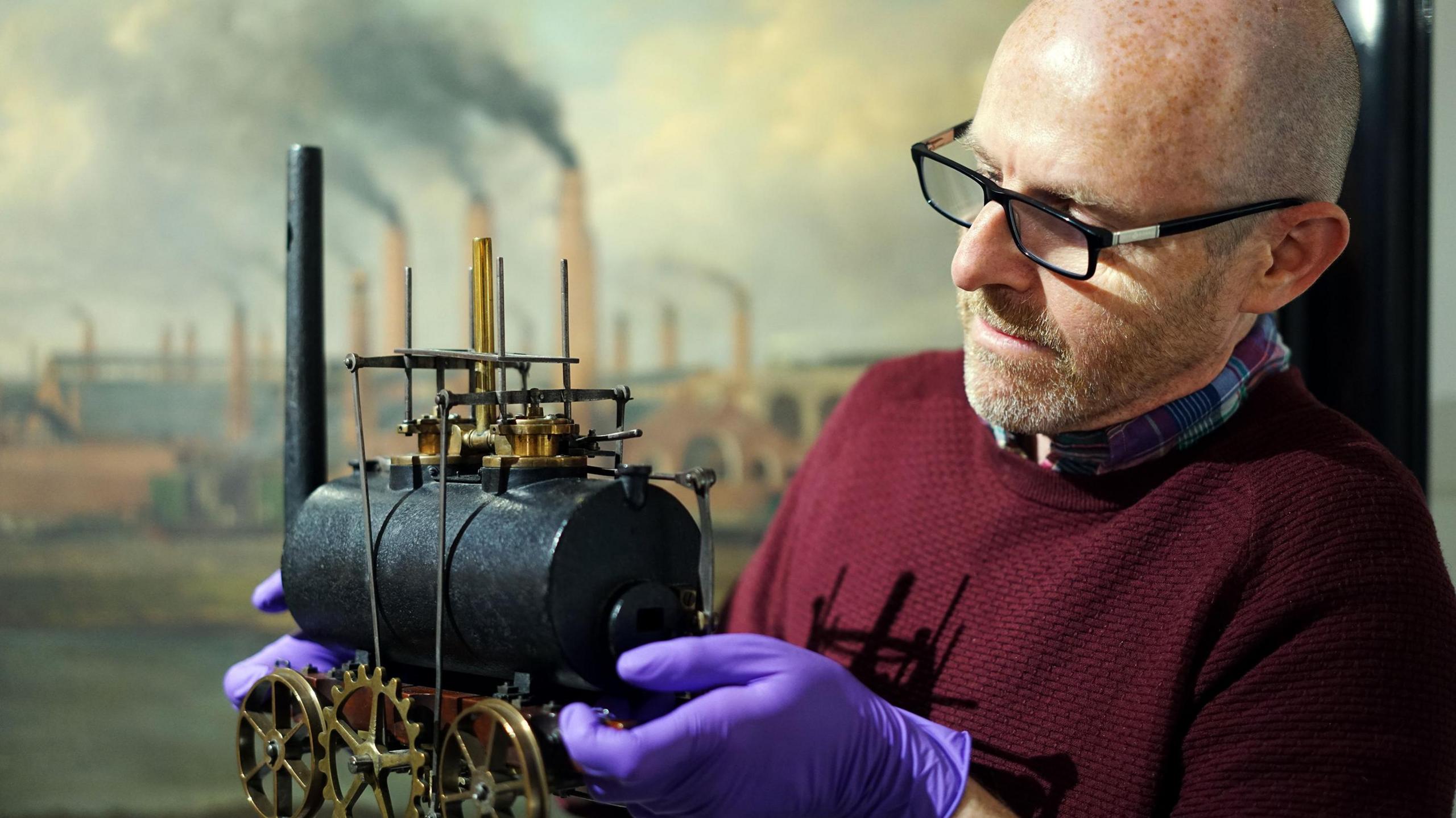 A man wearing purple latex gloves holding a model locomotive 