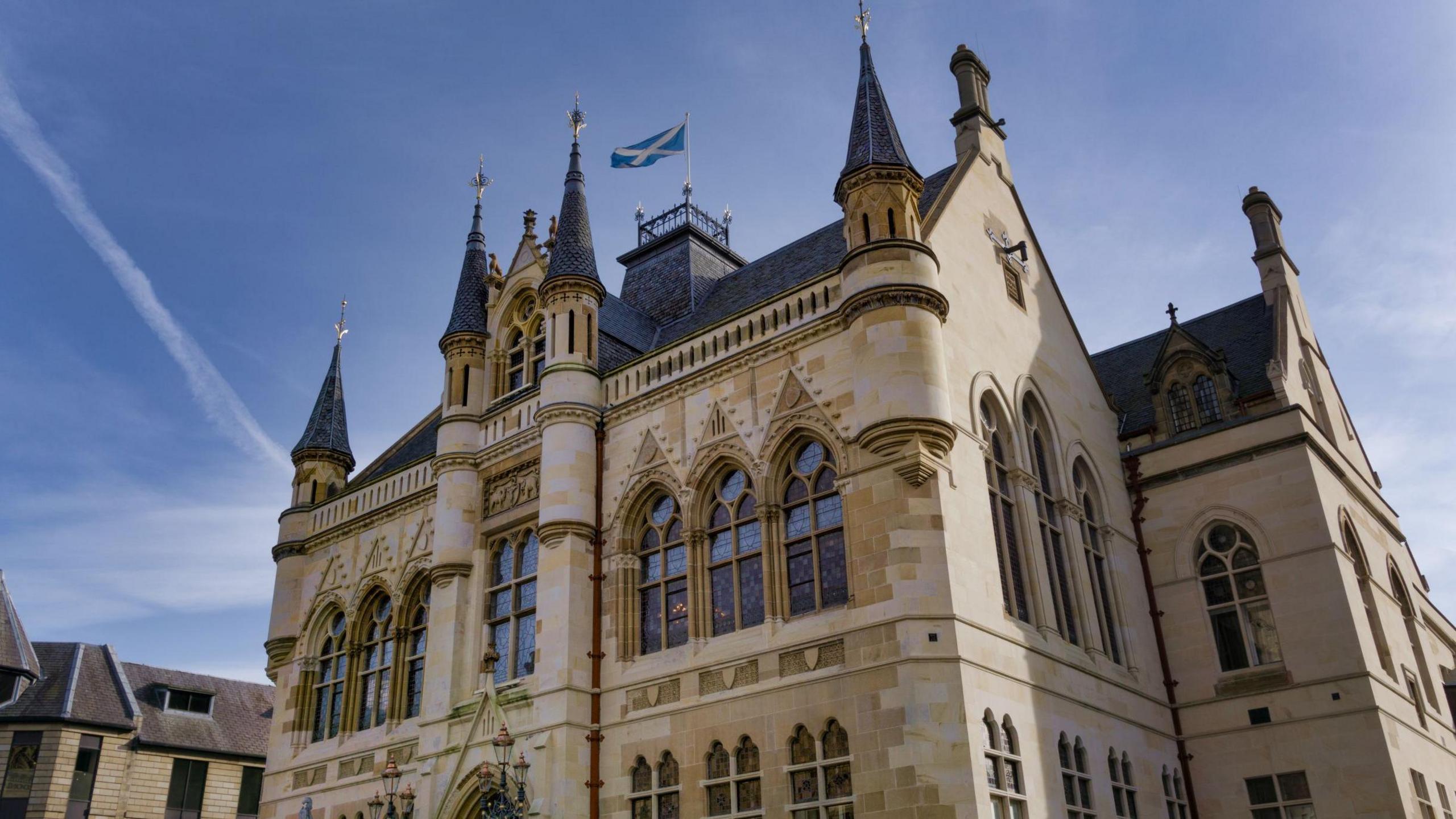 Built to a Flemish-Baronial style, Inverness Town House is a sandstone building with turrets and ornately designed windows. A Saltire flag flutters from a pole on the roof.