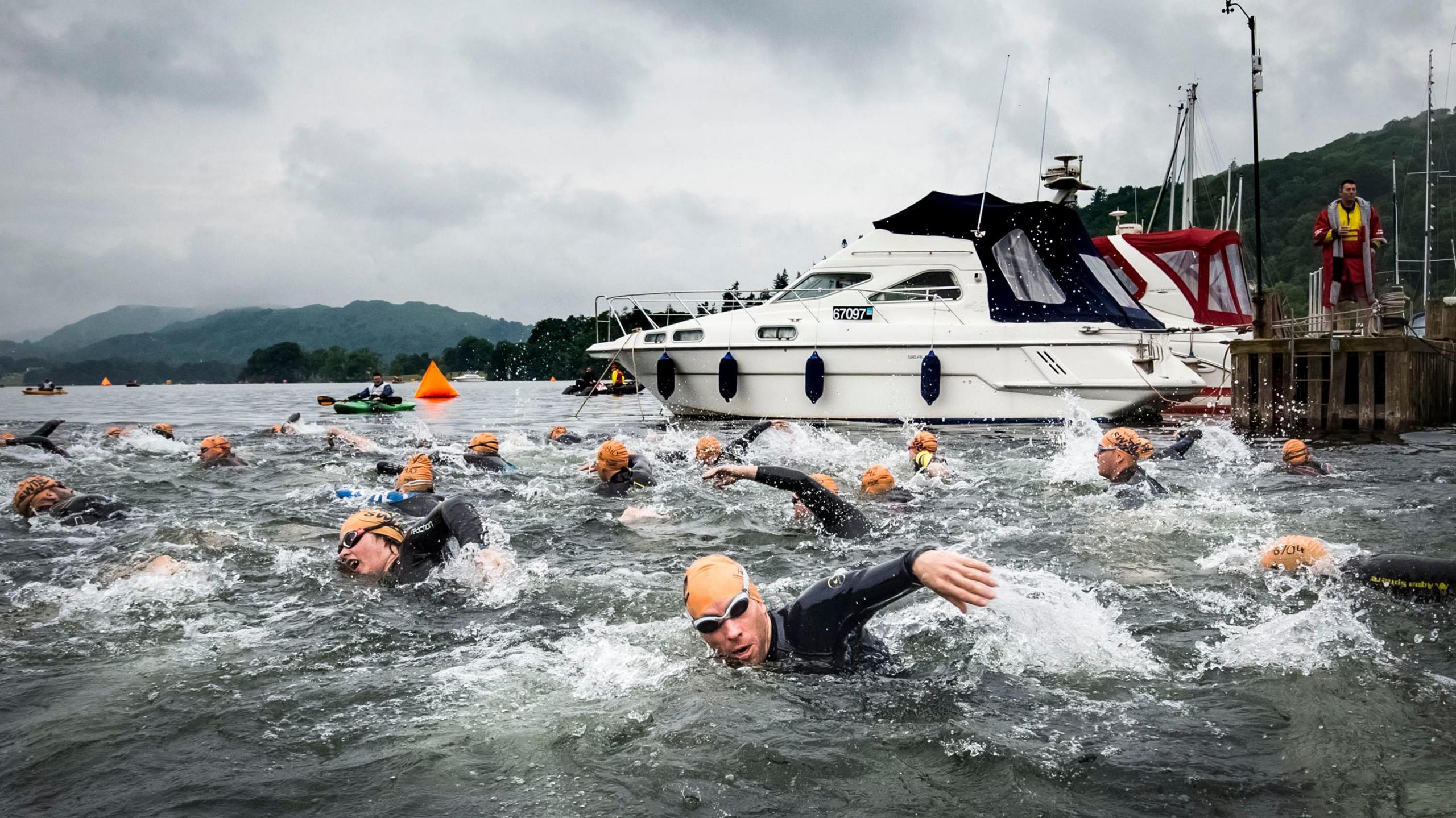 Swimmers in Lake Windermere, with a white boat on the lake in the background.