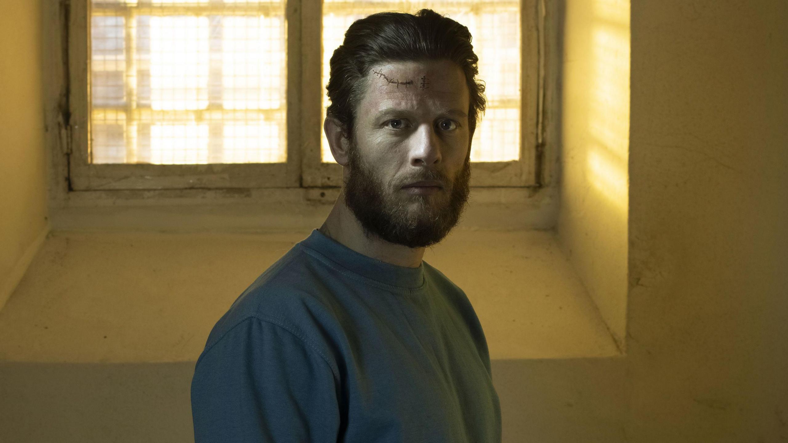 James Norton, in his role as Tommy Lee Royce in Happy Valley, standing in front of a prison cell window.