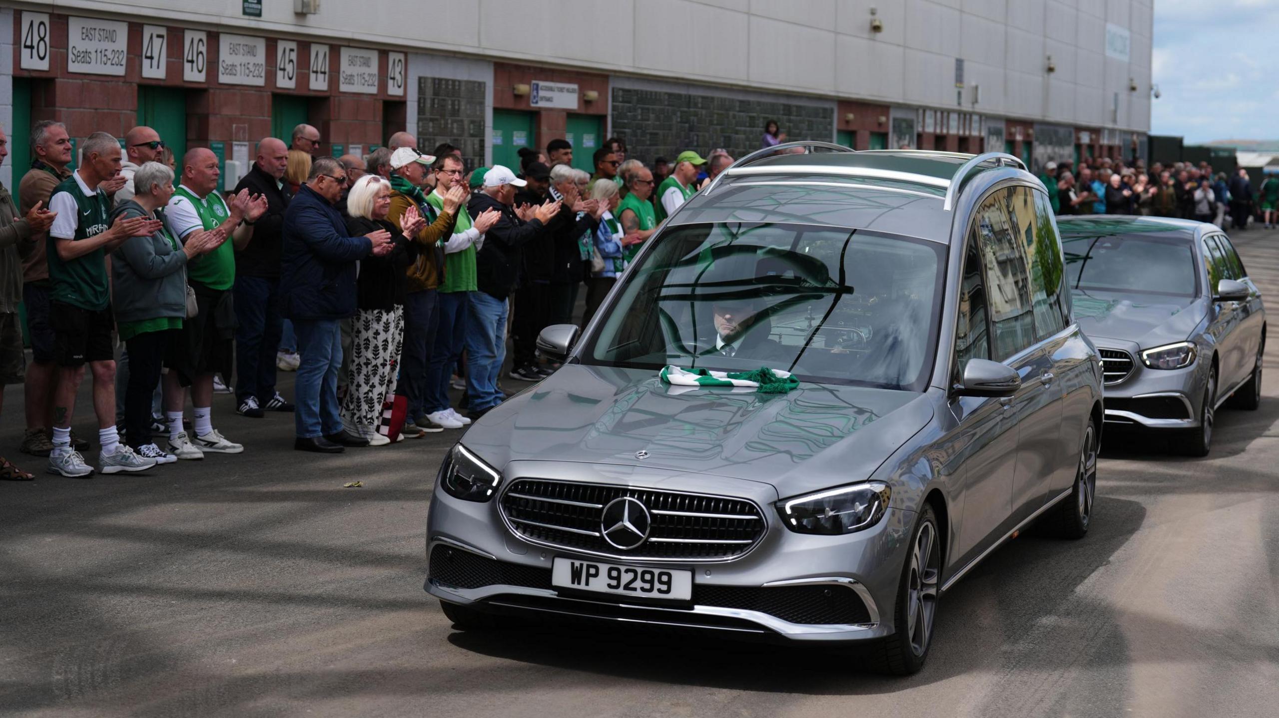 A silver hearse with the coffin of Sir Tom Farmer drives past supporters gathered outside Easter Road Stadium in Edinburgh