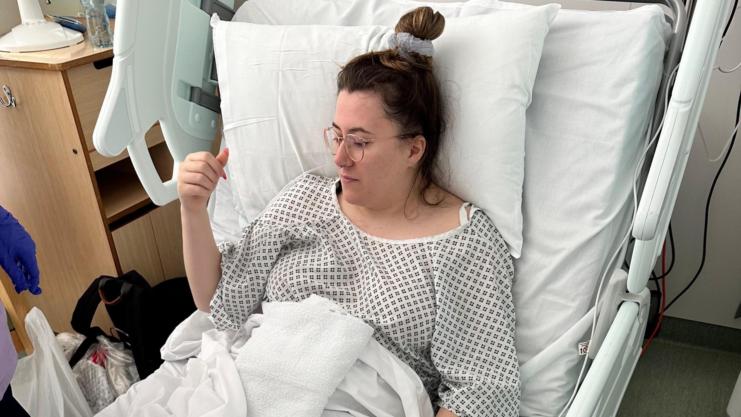 Natasha Reynolds sat up in a hospital bed for an operation to remove her cancerous ovary. She is wearing a gown, glasses and has her hair tied up