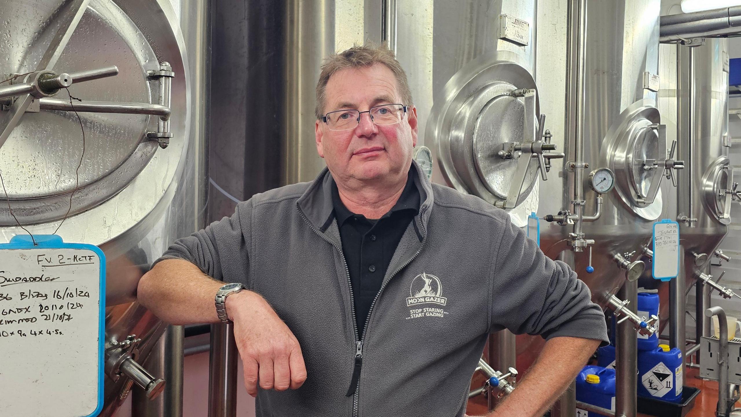 David Holliday leaning onto one of the fermenters at his brewery. Several other stainless steel fermenters can be seen behind him.