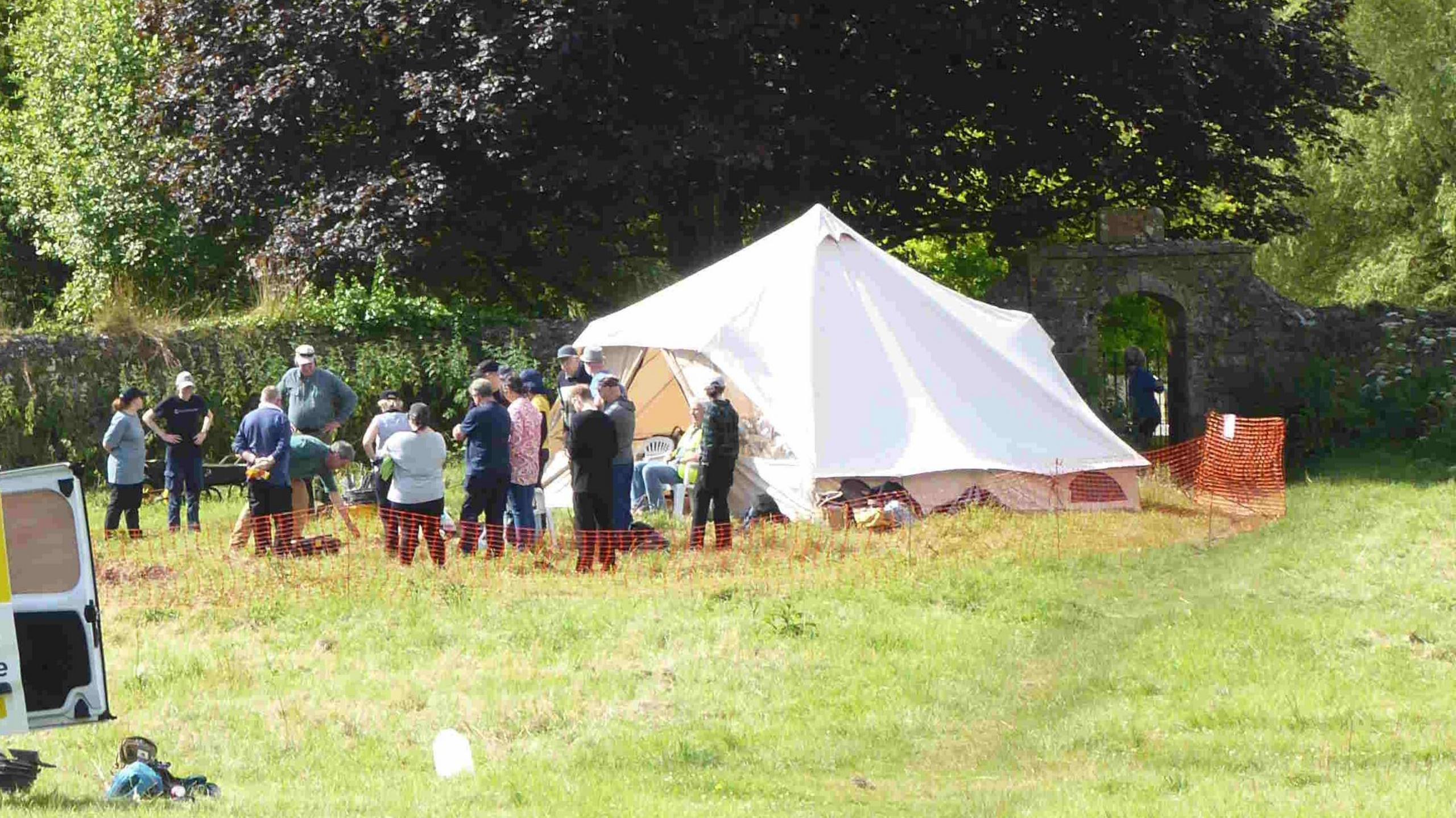 A group of people standing in a field next to a large white bell tent.