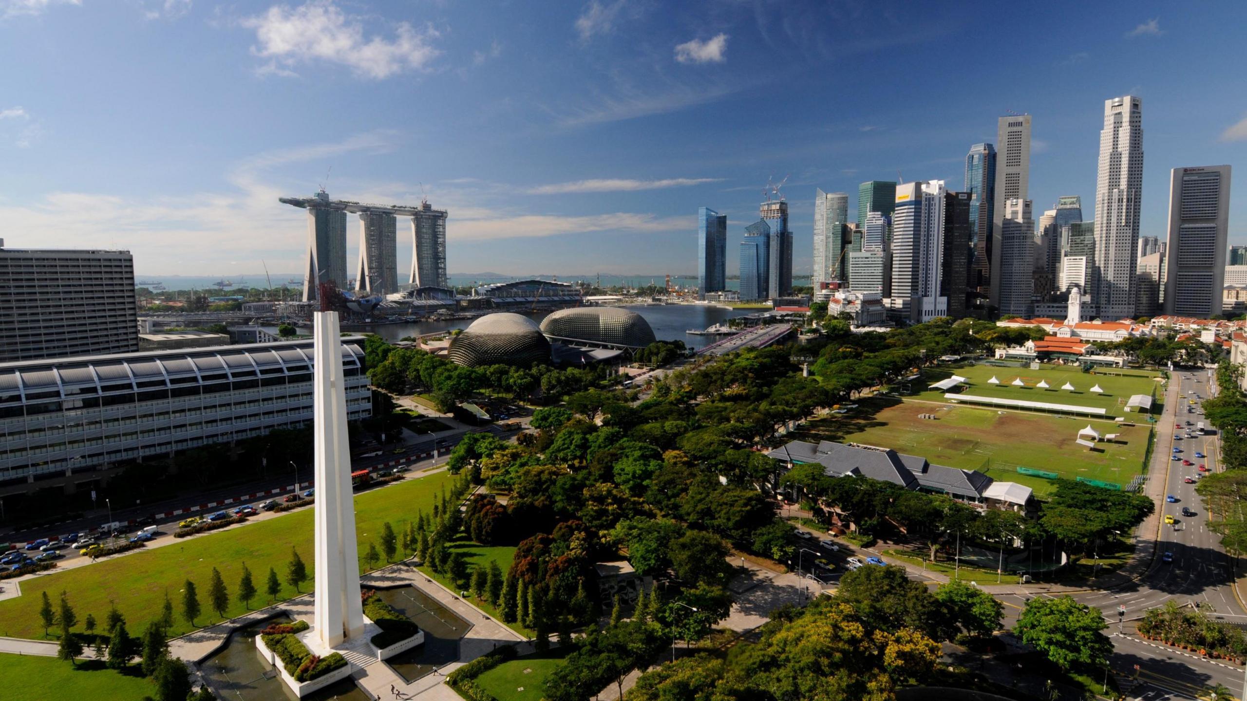 A wide view of Singapore's skyline with green space and trees in the foreground and blue sky in the background