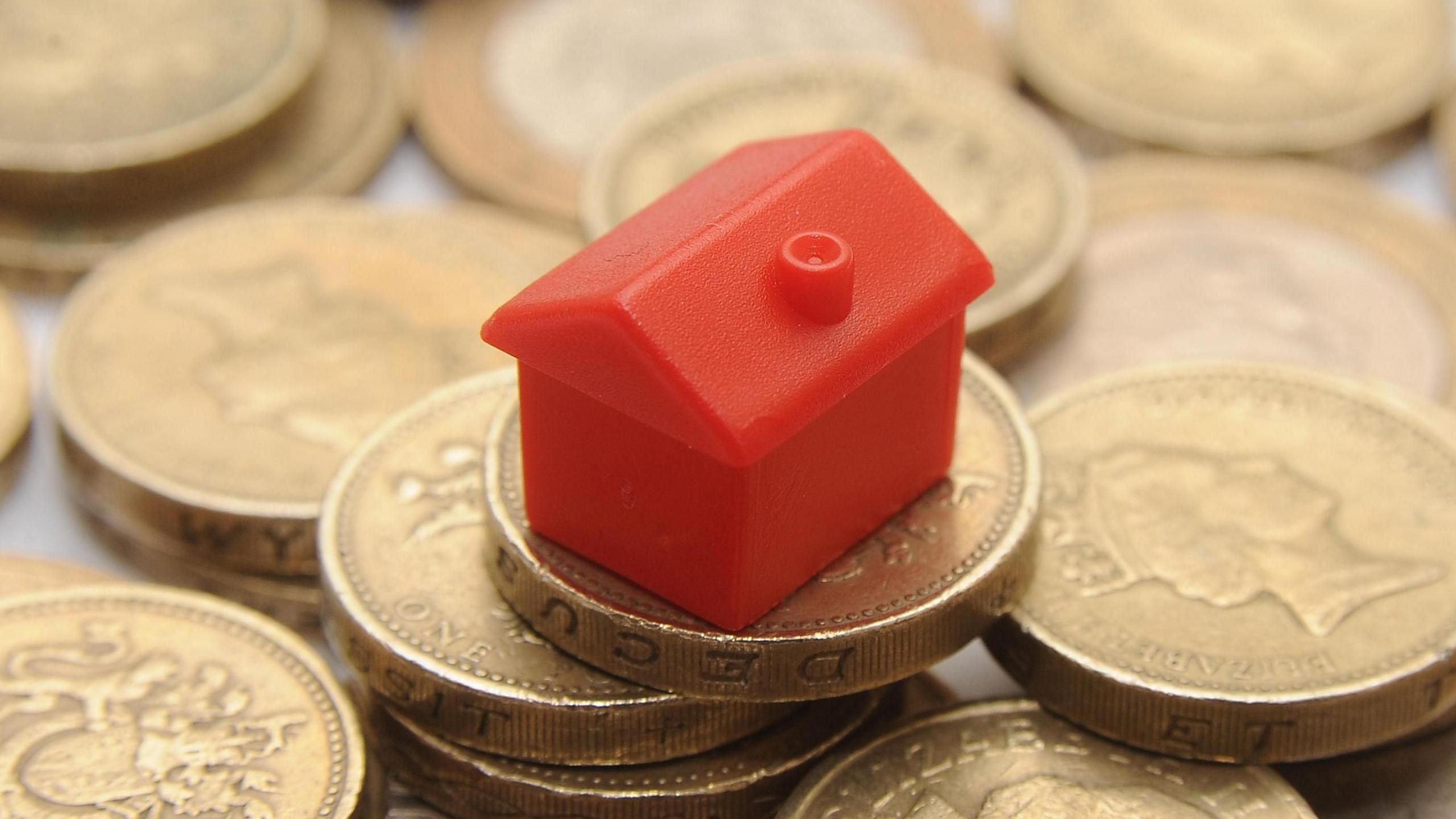 A picture of a red model house from the board game Monopoly sat on a pile of pound coins