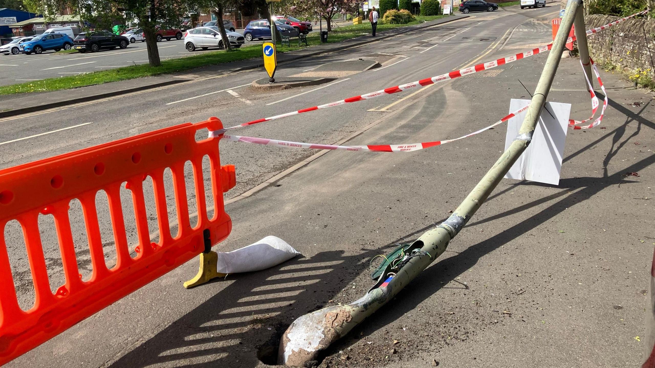 A lamppost has been flattened onto the pavement and is cordoned off by red tape and a red bollard
