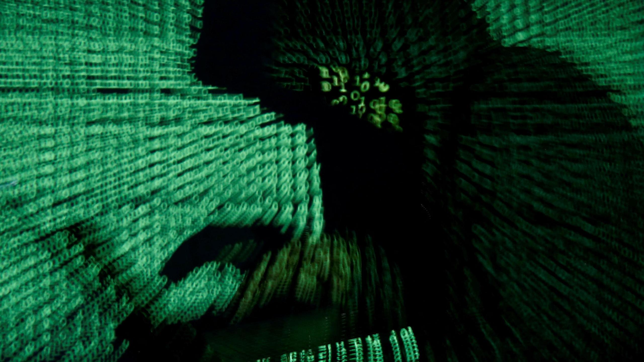 A man holds a laptop computer as green cyber code is projected on him.