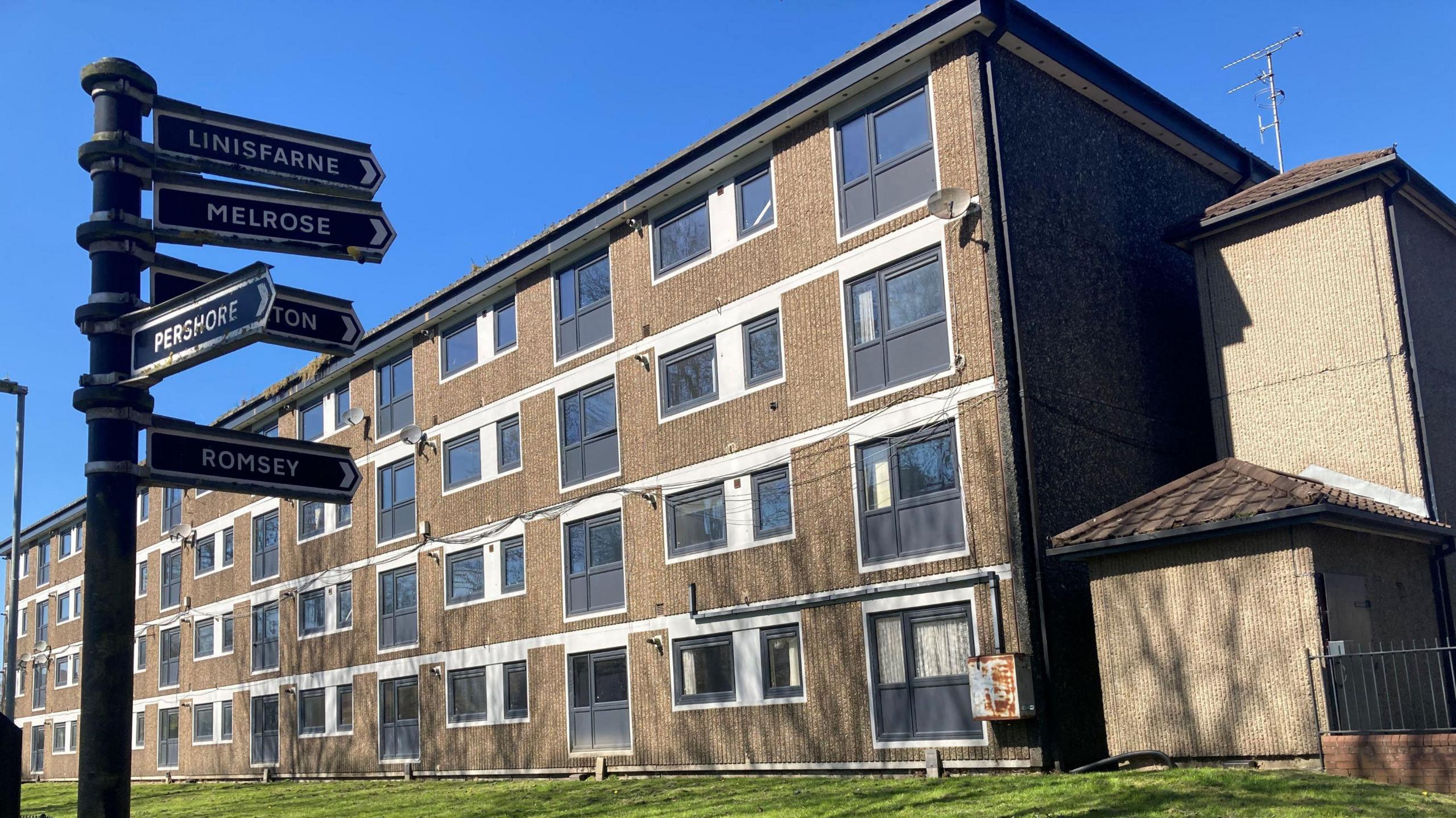 The Lower Falinge estate in Rochdale. A 1970s four-floor brick block of flats. A blue sign offers directions to each of the blocks