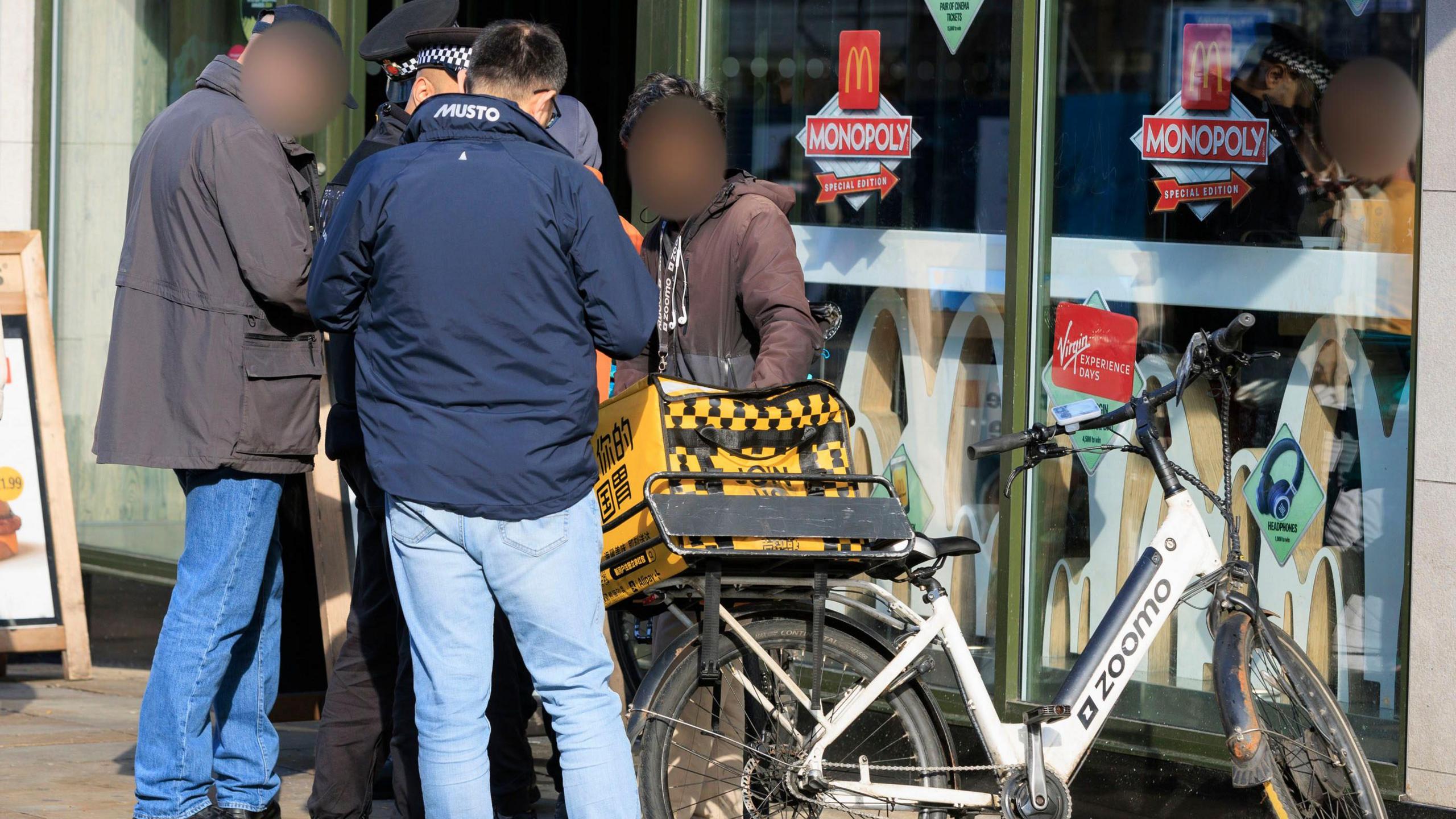 Four people including a police officer in uniform are talking to someone standing next to an e-bike outside a McDonalds restaurant.