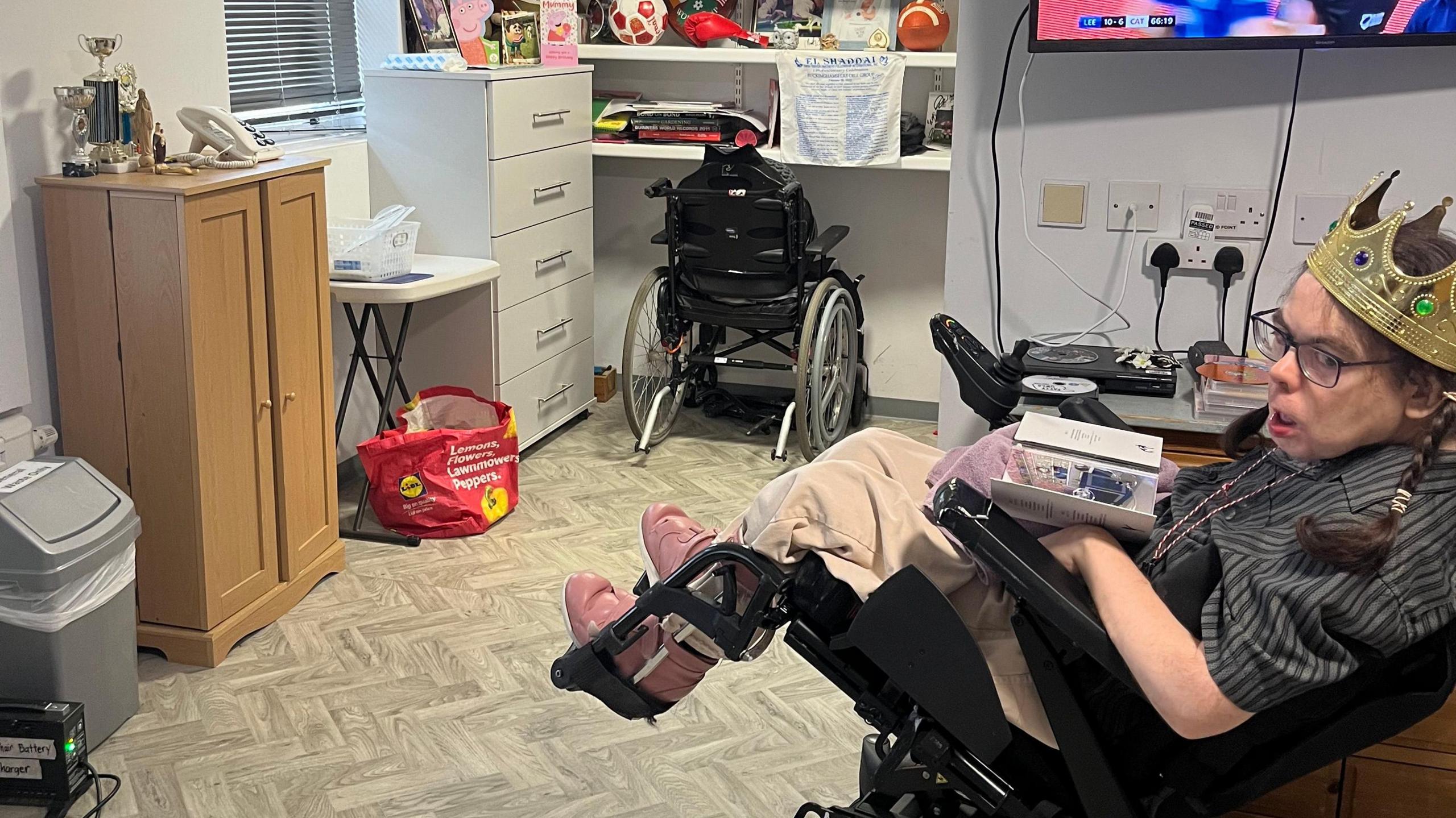 A person in a wheelchair wearing a crown, in a newly-renovated bedroom