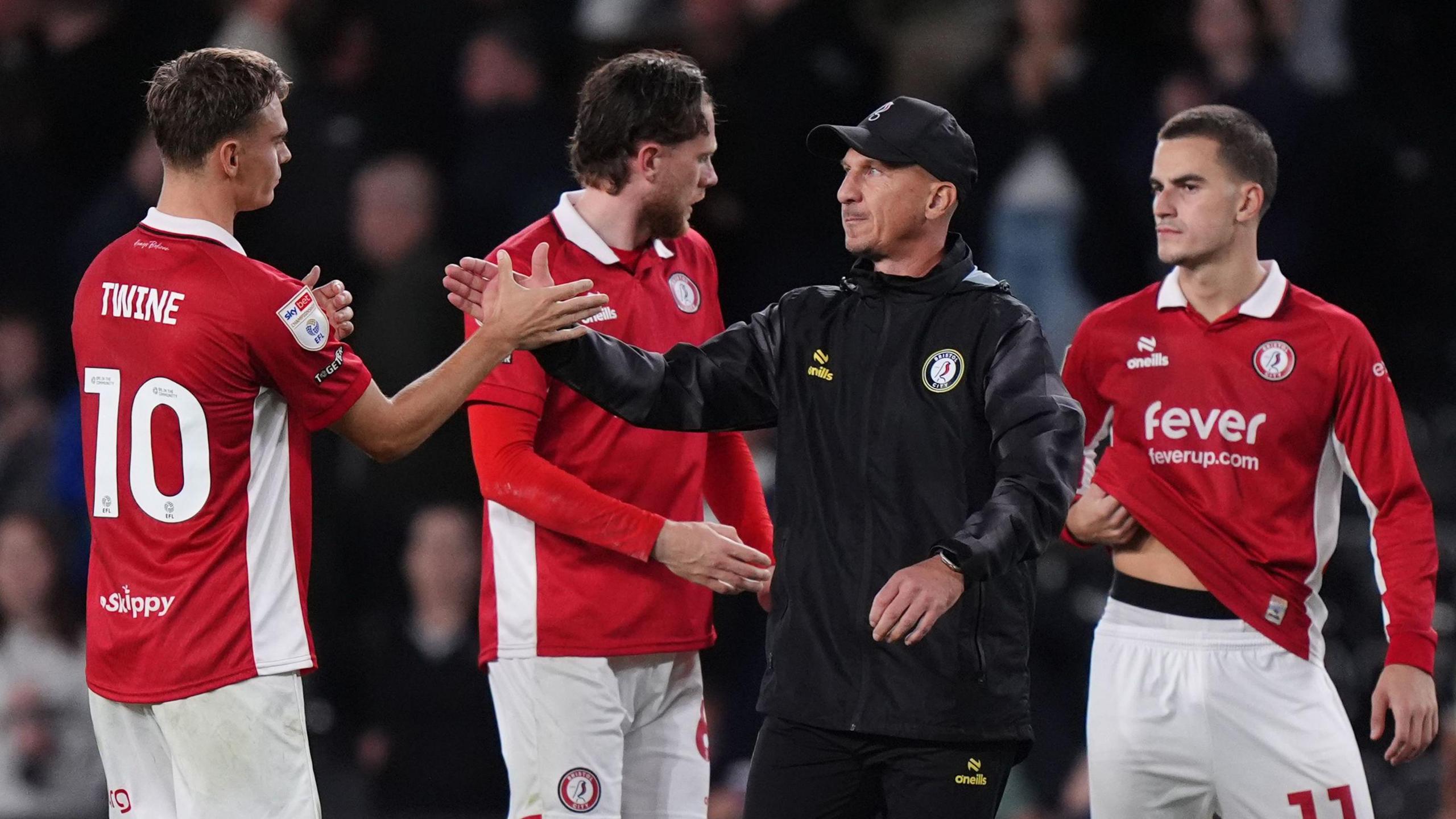 Gerhard Struber claps hands with Scott Twine (left) after full-time as Rob Dickie stands behind and Anis Mehmeti holds his hand under his shirt also behind him