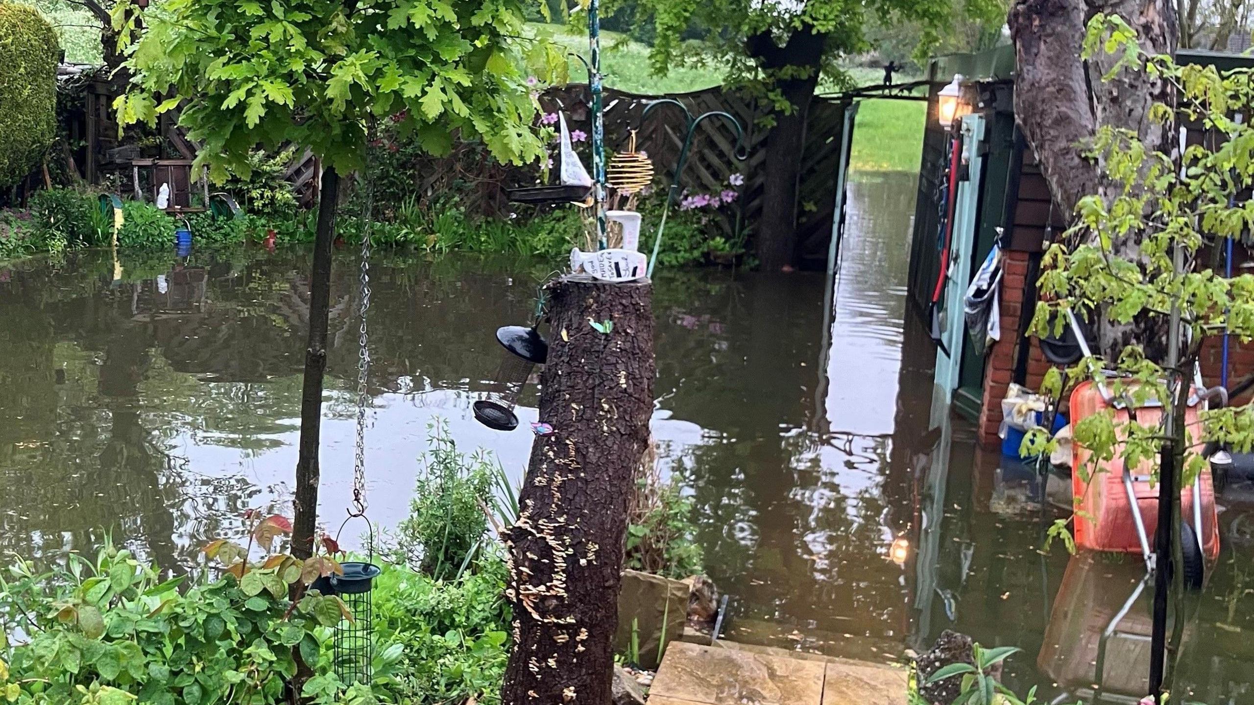 A waterlogged garden, with paving slabs under water, which leads onto a field which also has water on it