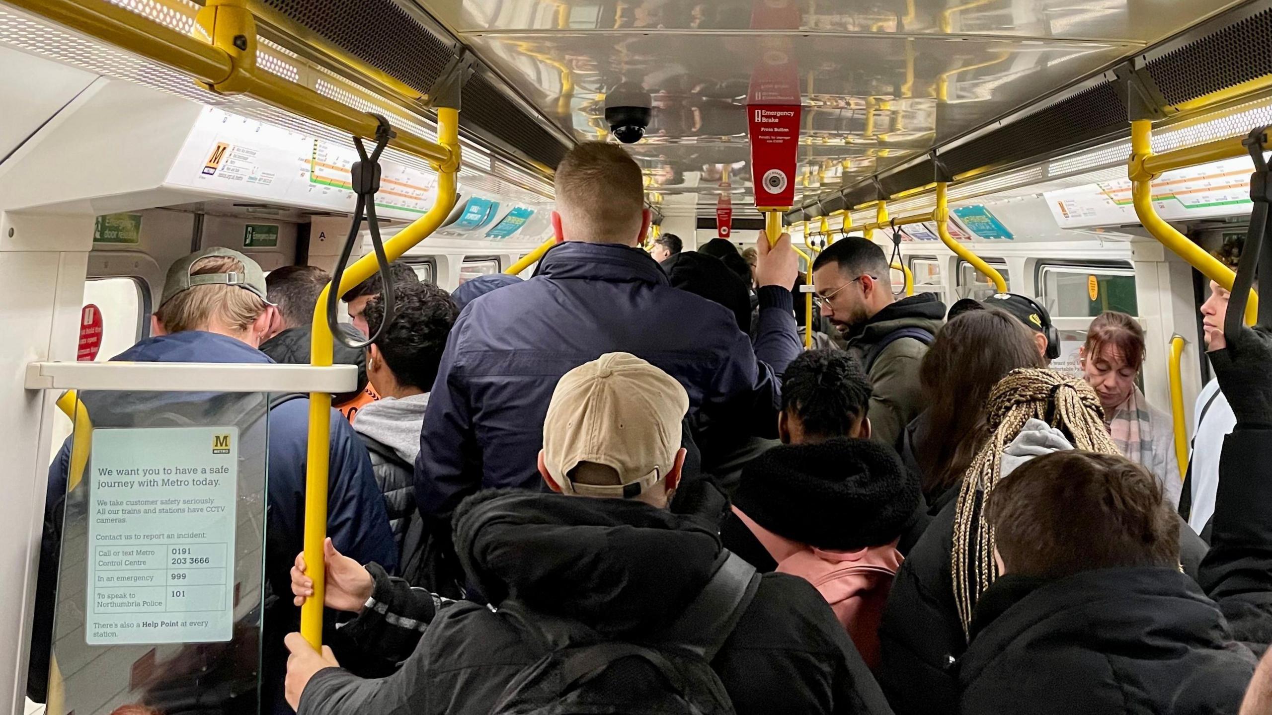 A yellow and white Metro carriage is full of people on their commute.