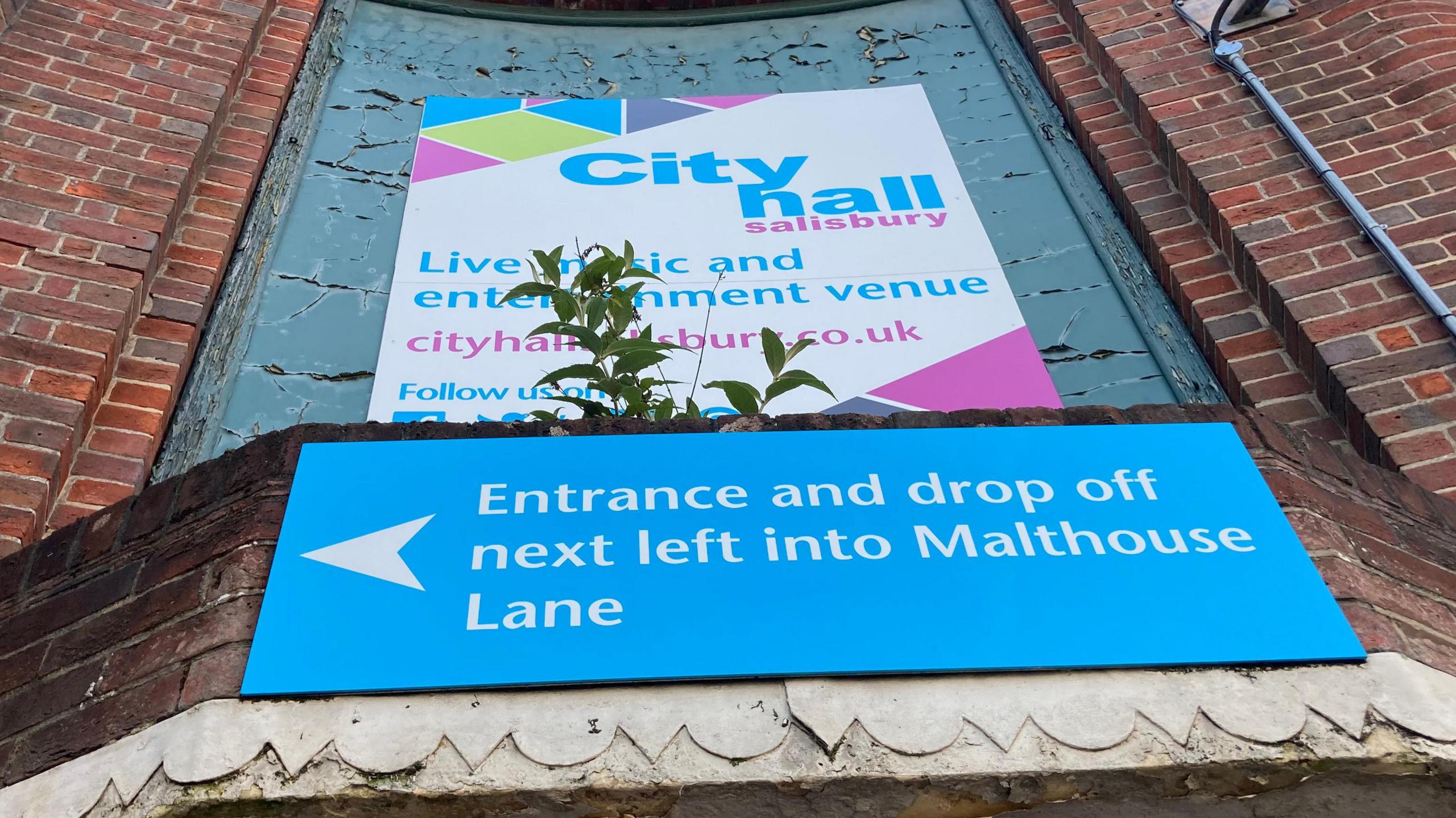 A photo showing signs for the City Hall in Salisbury. One points visitors towards the main entrance and is white writing on a light blue background