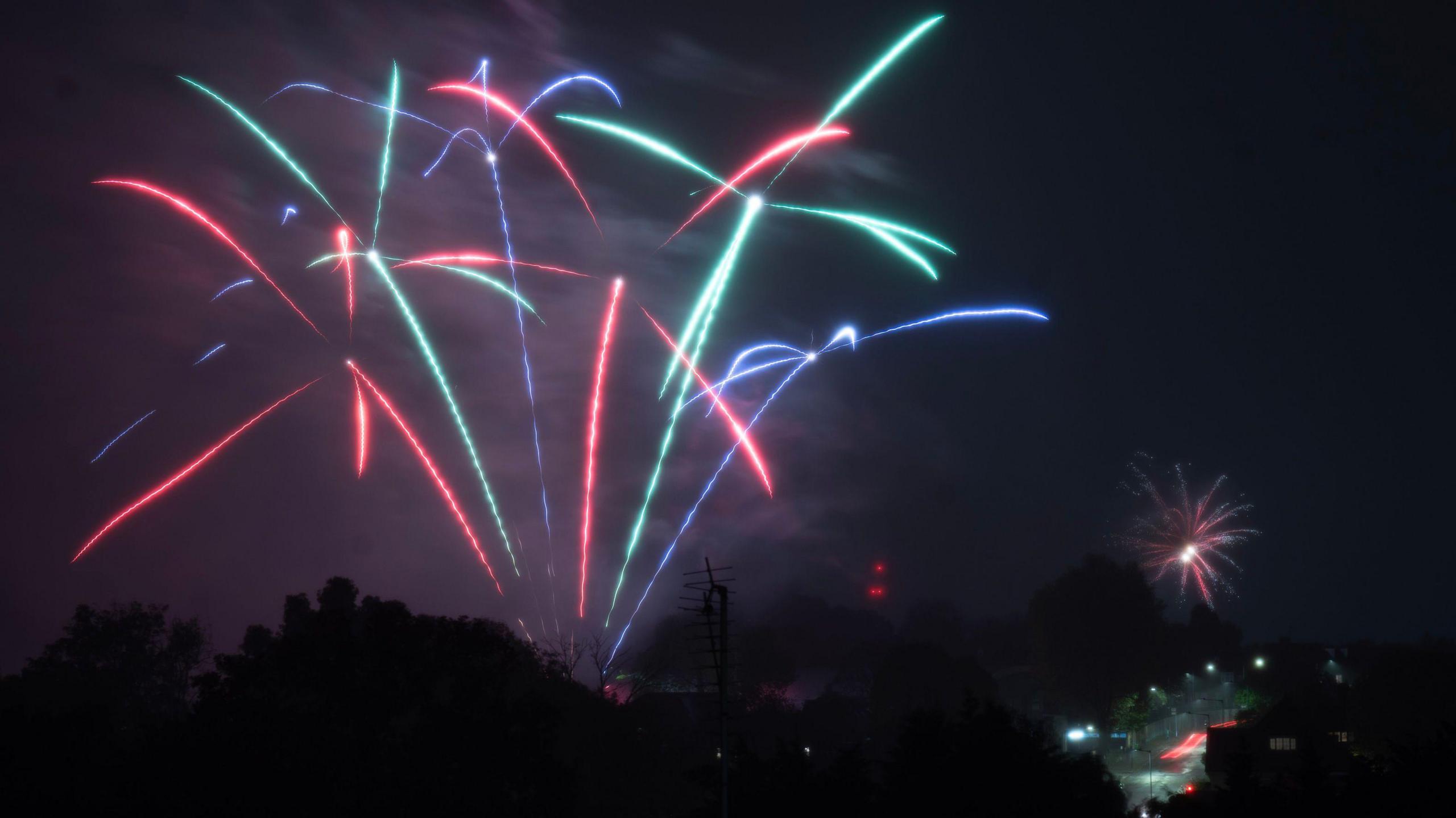 A mixture of green, red and indigo fireworks in the sky as people celebrate Bonfire night