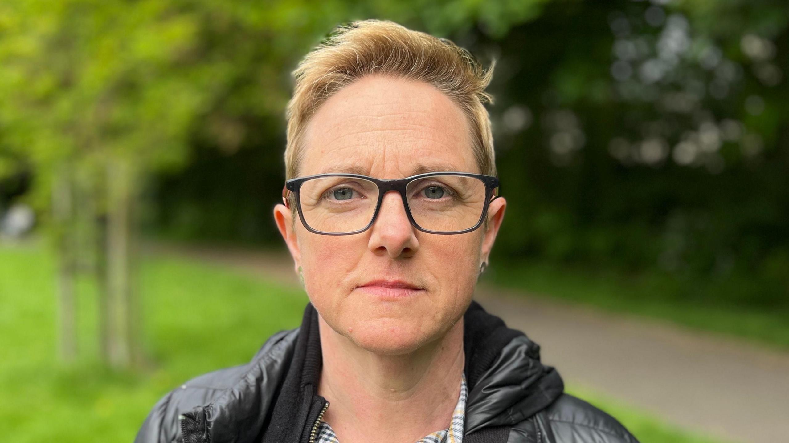 Roz Adams, who has short blonde hair, glasses and a black puffy jacket, looks into the camera