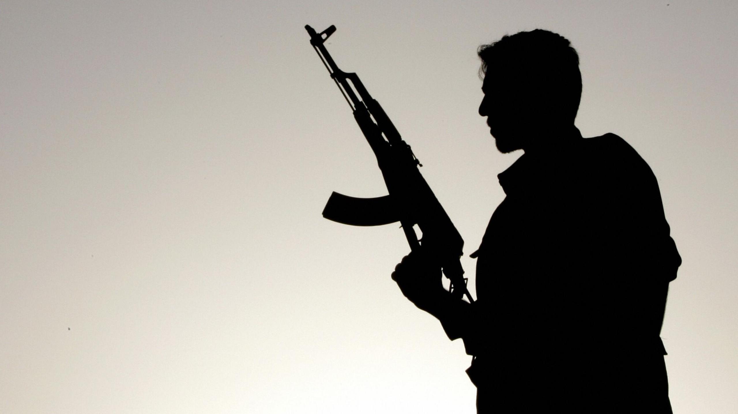 A PKK fighter holding an assault rifle silhouetted against the Sun