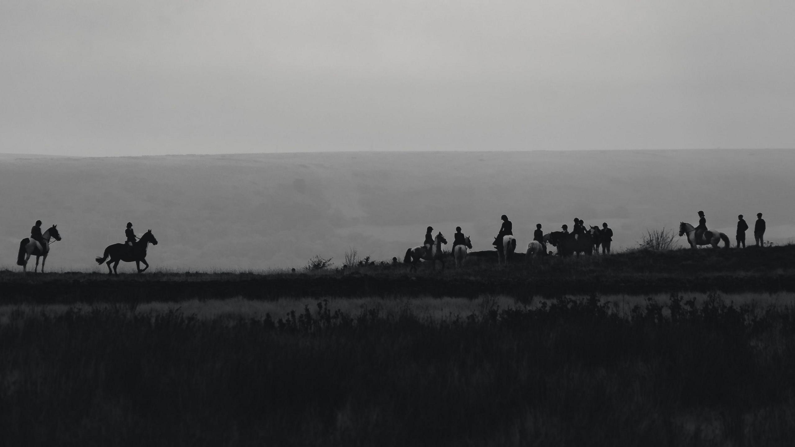 A black and white photo of a hunt, silhouetted against the sky