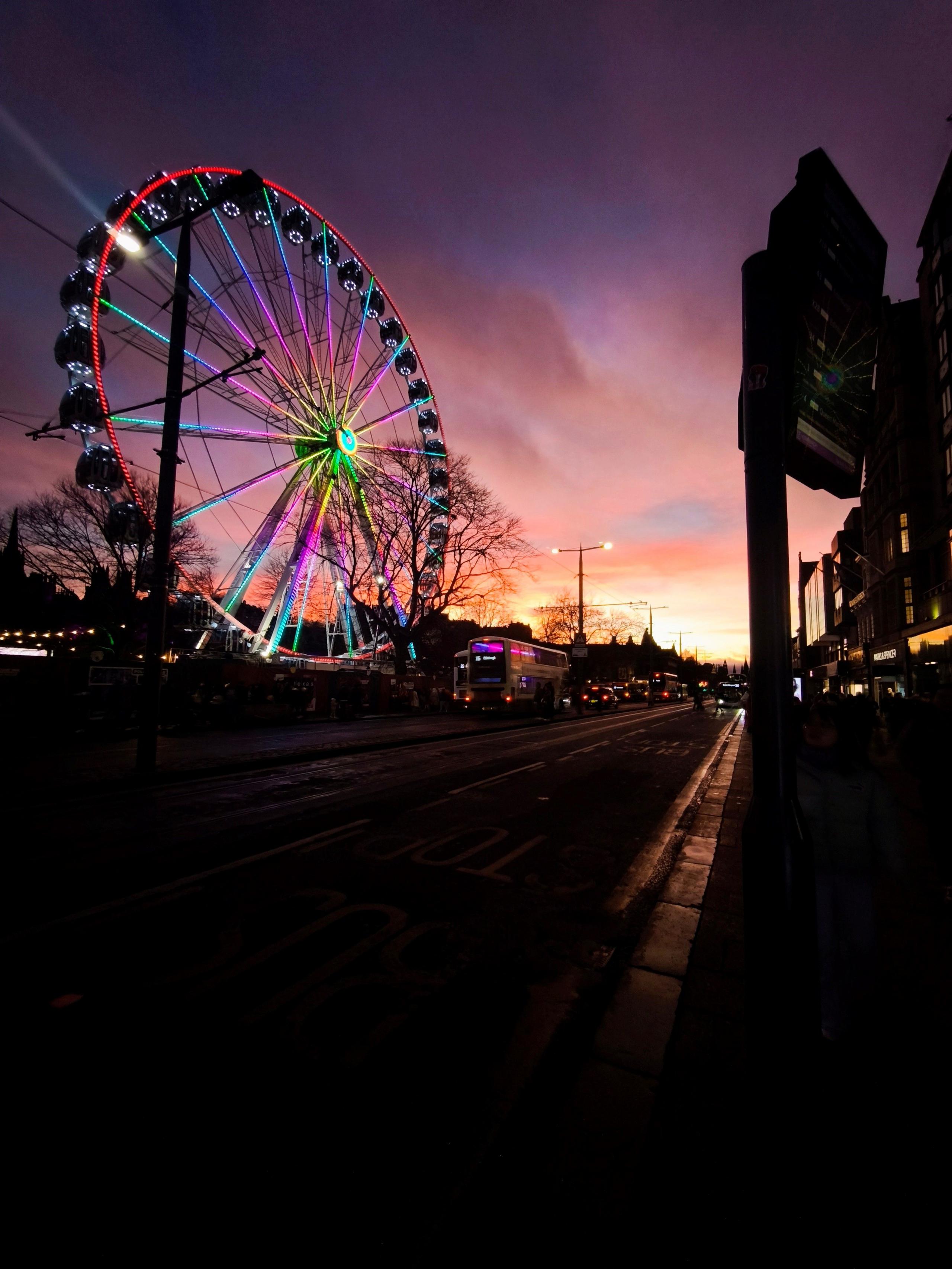 A ferris wheel lit up by the sun with the rest of the street in shadow