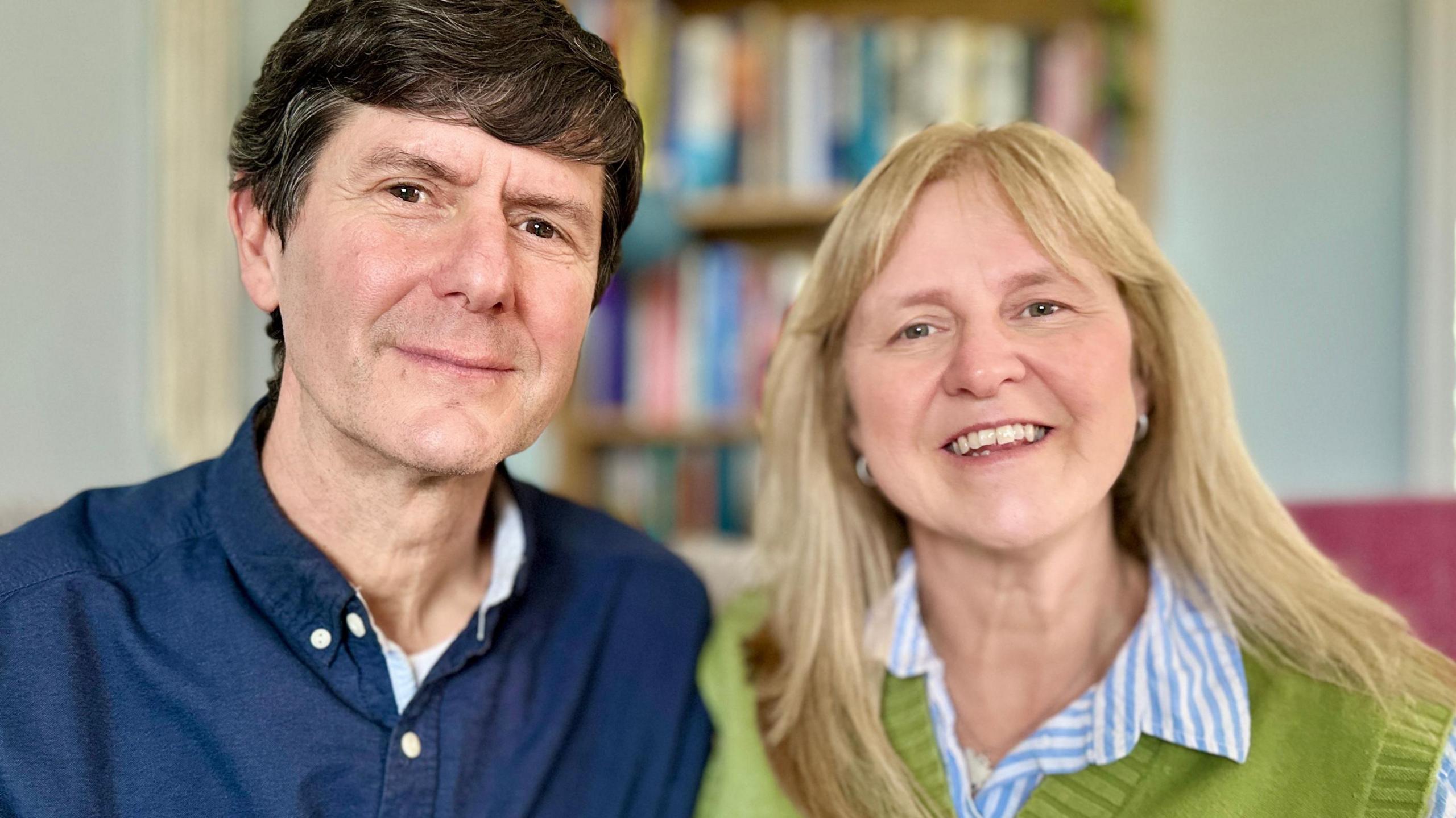 Portrait photo of Mark and Beverley Landreth-Smith, who have hosted seven different children over the last seven years. They are both smiling. Beverley is blonde with long hair and is wearing a green jumper over a blue and white striped shirt. Mark is wearing a navy blue shirt and has short, dark brown hair.