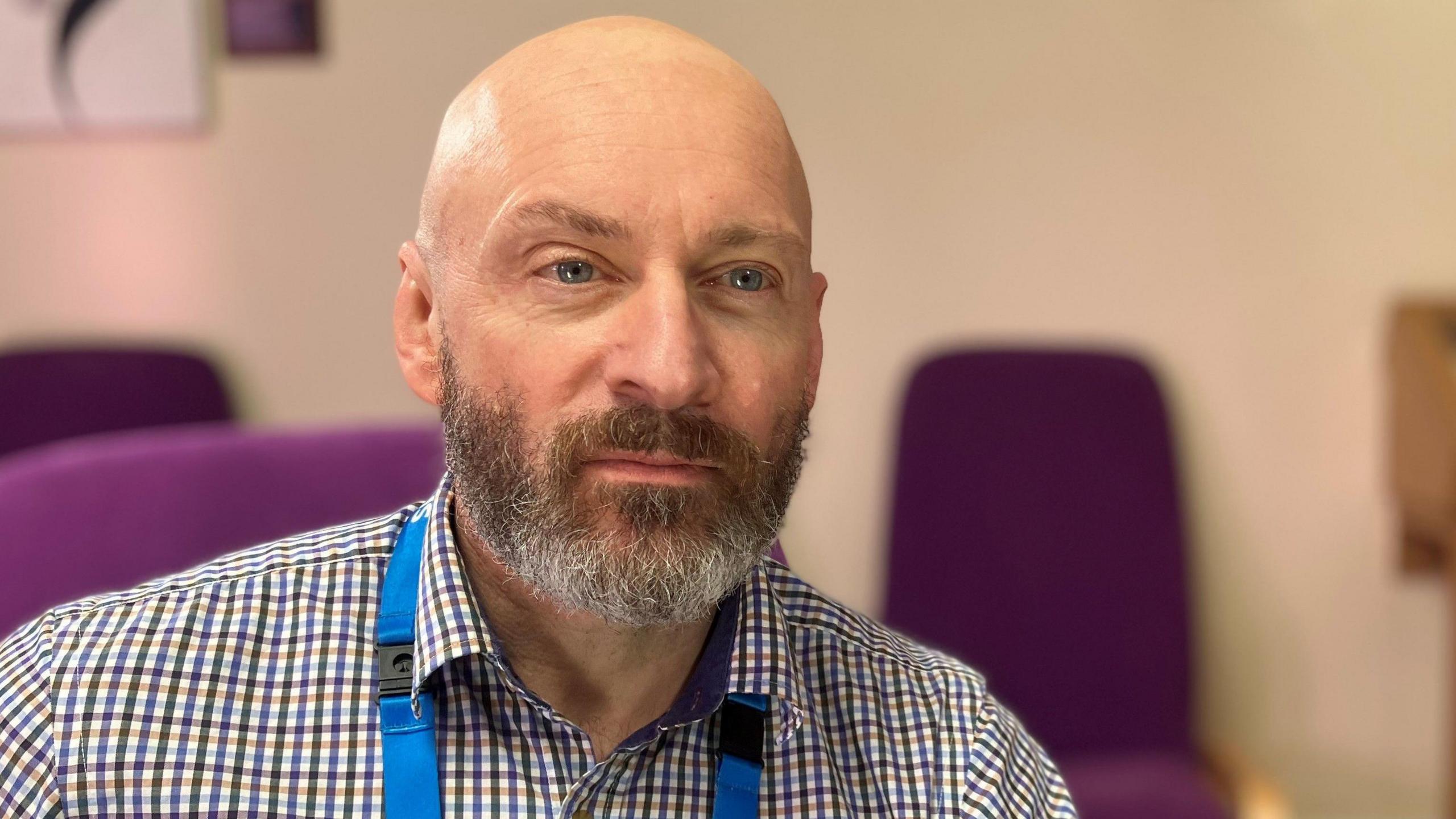 Dorian pictured in the offices of Derbyshire Healthcare NHS Foundation Trust wearing a checked shirt and an NHS lanyard.