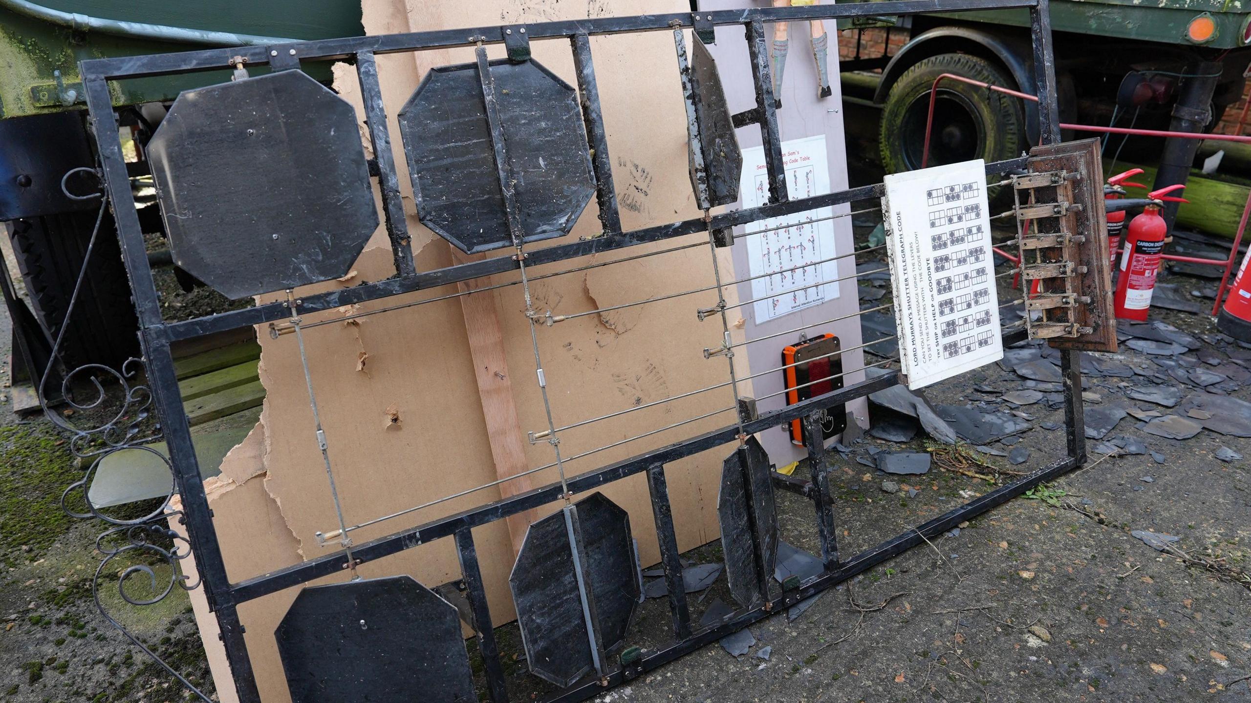 An interactive element from the museum, in this case a black steel grid with spinning disks in the spaces, is laying on its side outside the museum. It is covered partly n white ash.