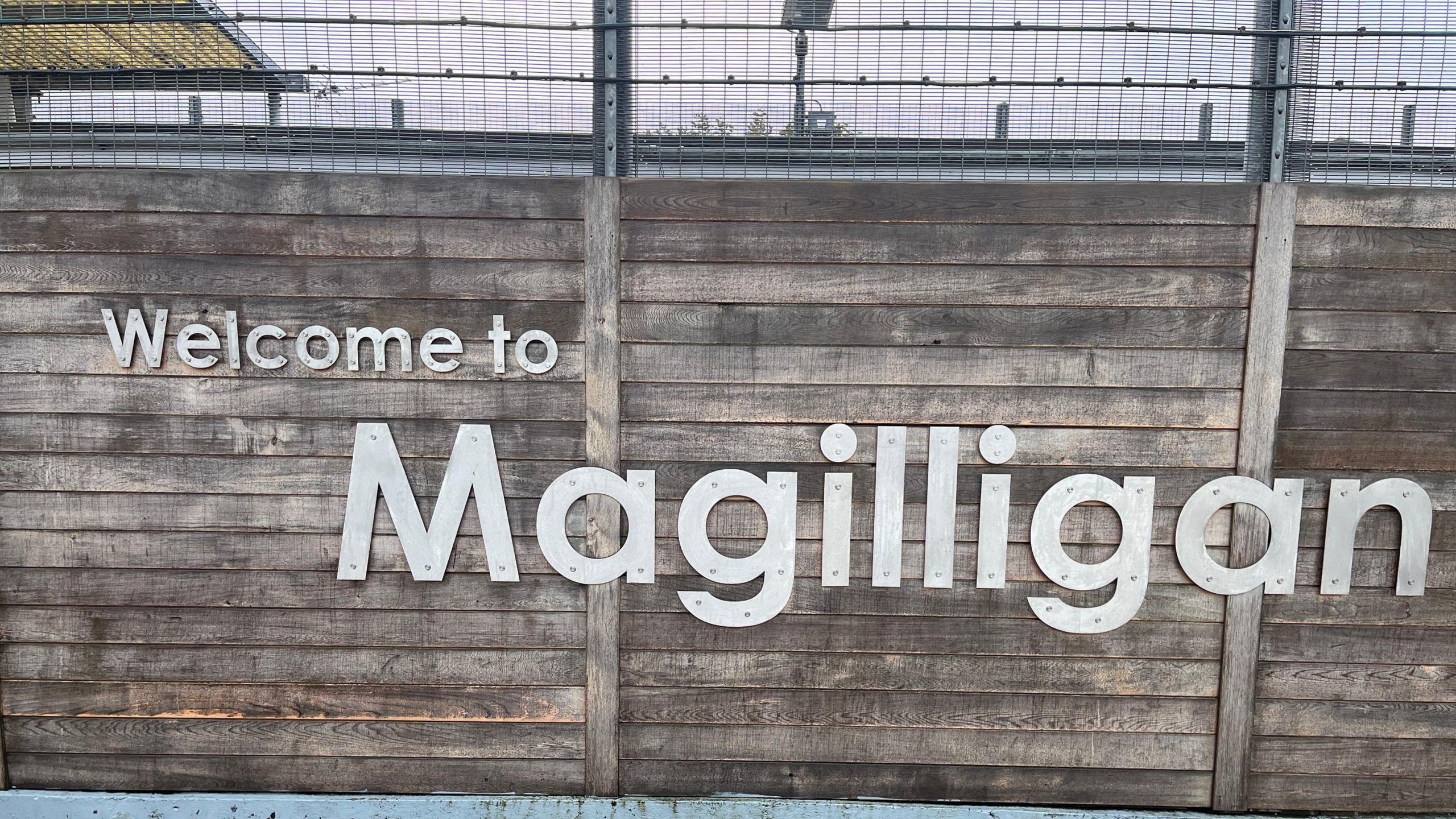 'Welcome to Magilligan' sign on wood fencing.