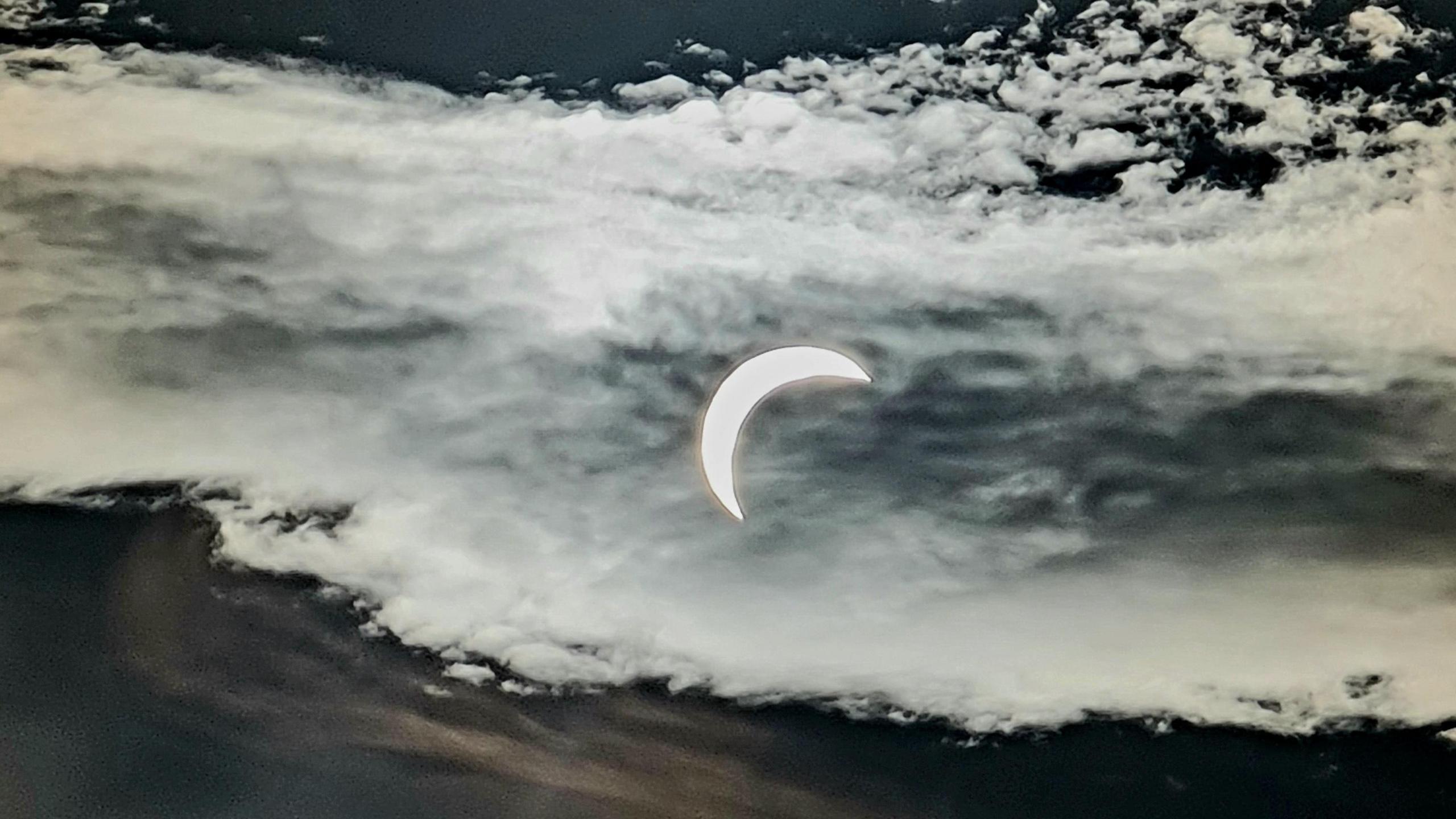 A semi-circled-shaped sun in the night sky against a backdrop of clouds.