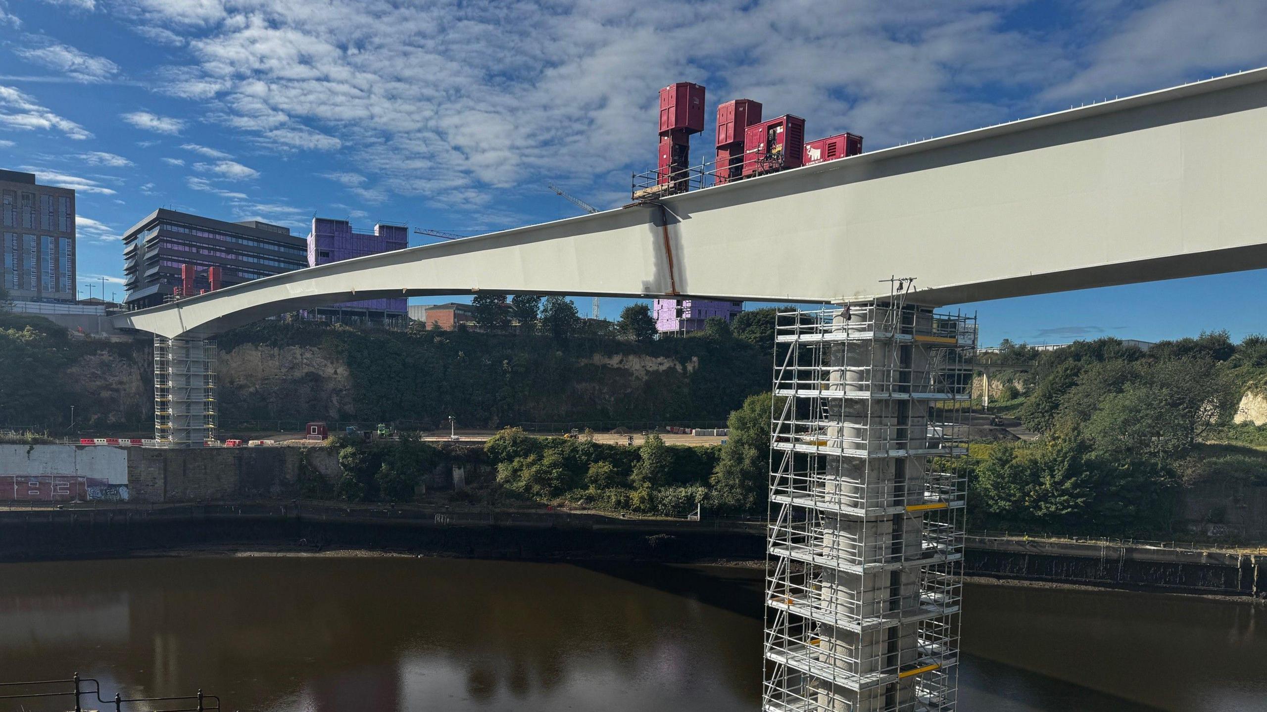 A shot of the bridge from the river bank. The joint between the right section of the bridge and the middle section can be clearly seen. Scaffolding has been erected around the bridge's supports.