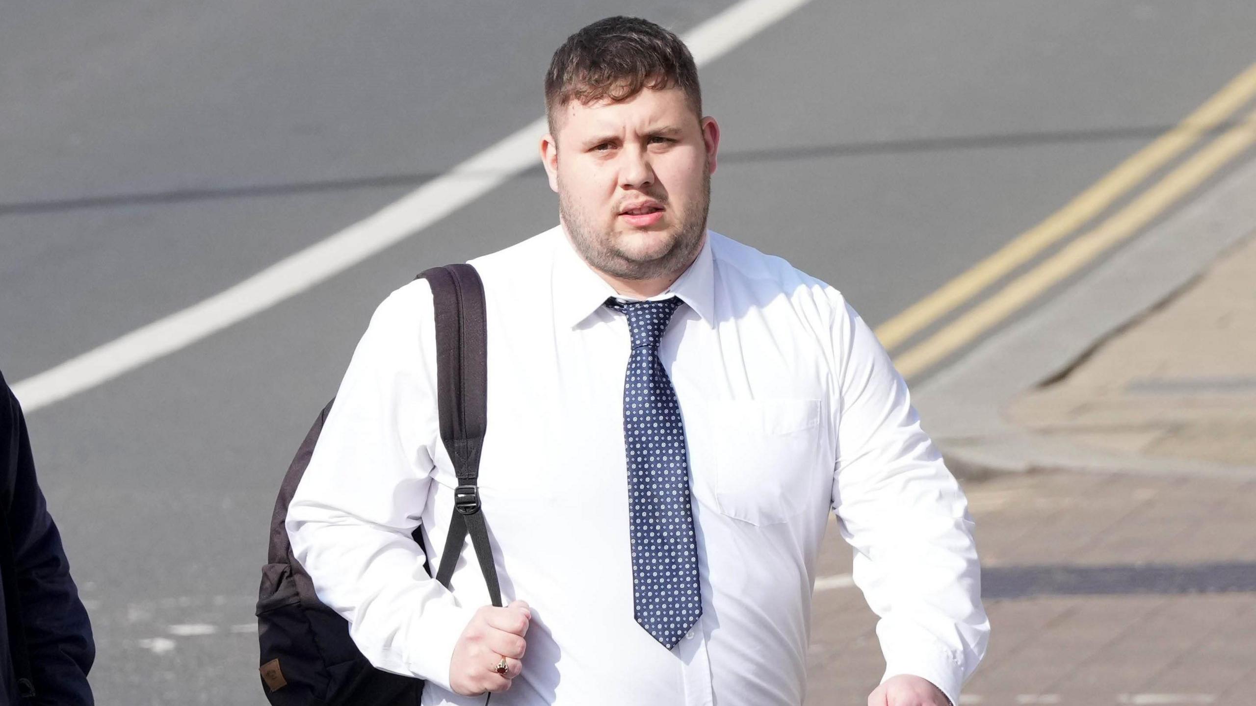 A man in a white shirt and blue tie with a backpack over his shoulder.