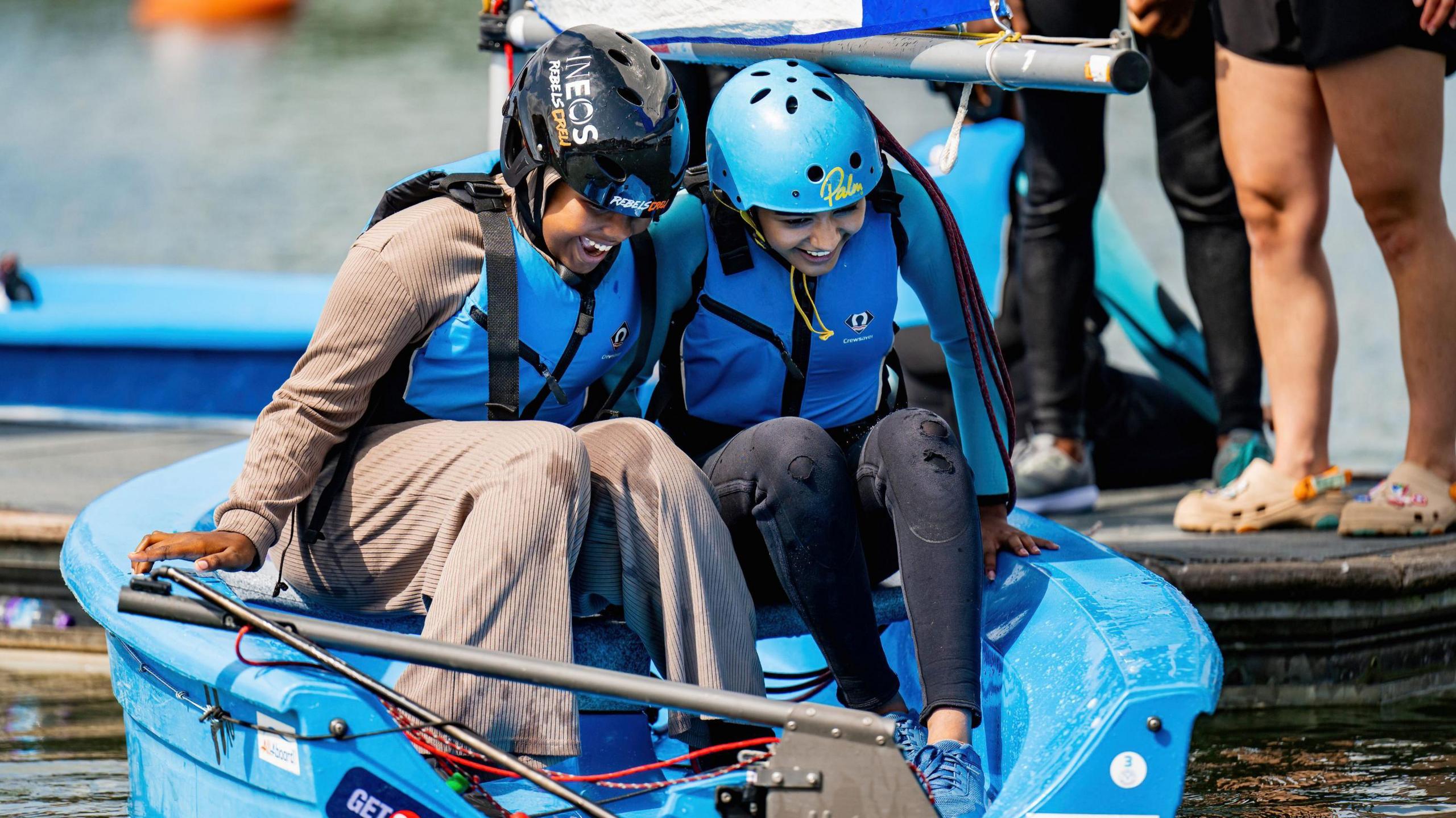 Two young girls in blue life jackets and hats, smiling on a blue boat