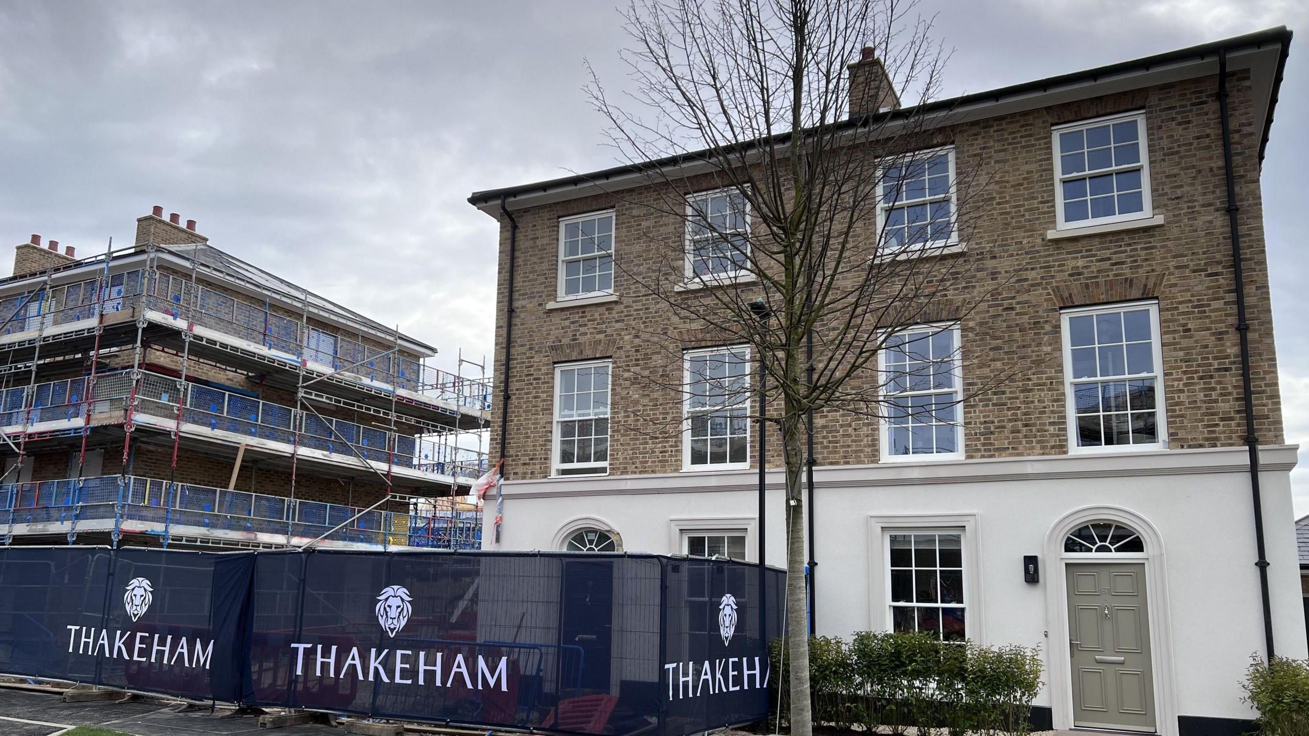 Picture shows a completed three bed house with a green door and Thakeham hoarding around the house next door.