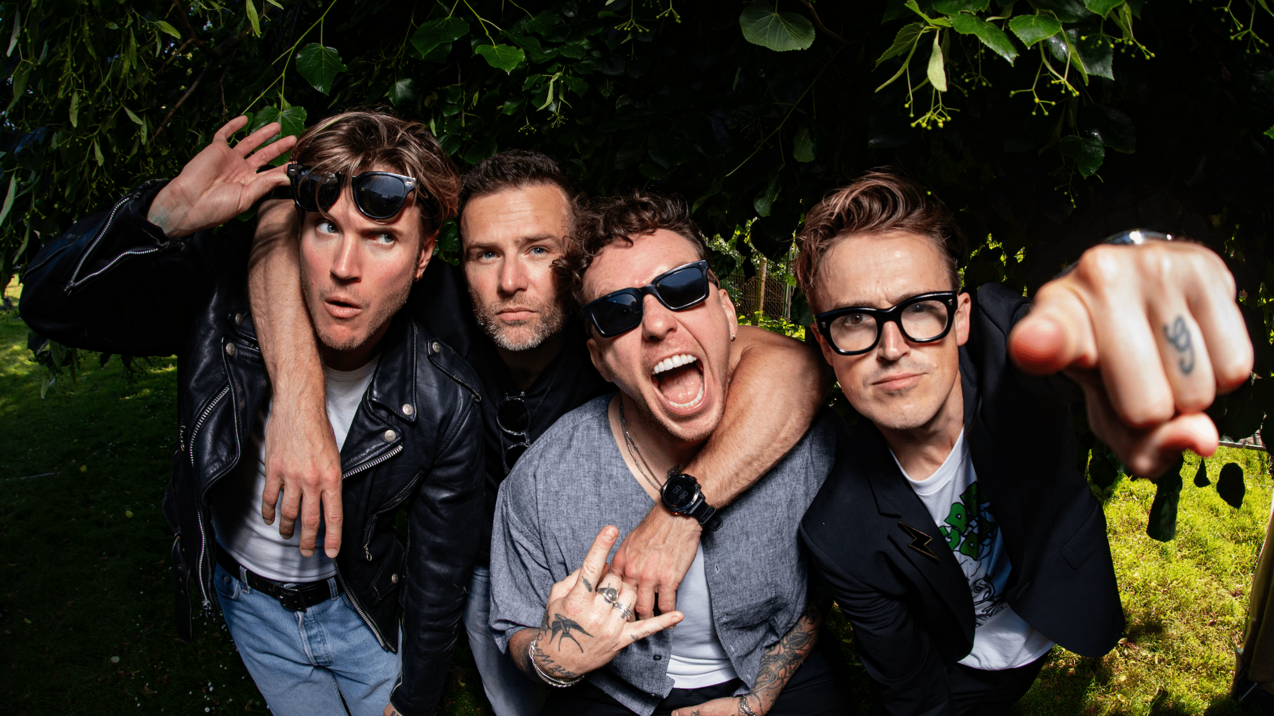 Mcfly band members - Dougie Poynter, Harry Judd, Danny Jones and Tom Fletcher.  They are all hugging and stood in front of greenery.