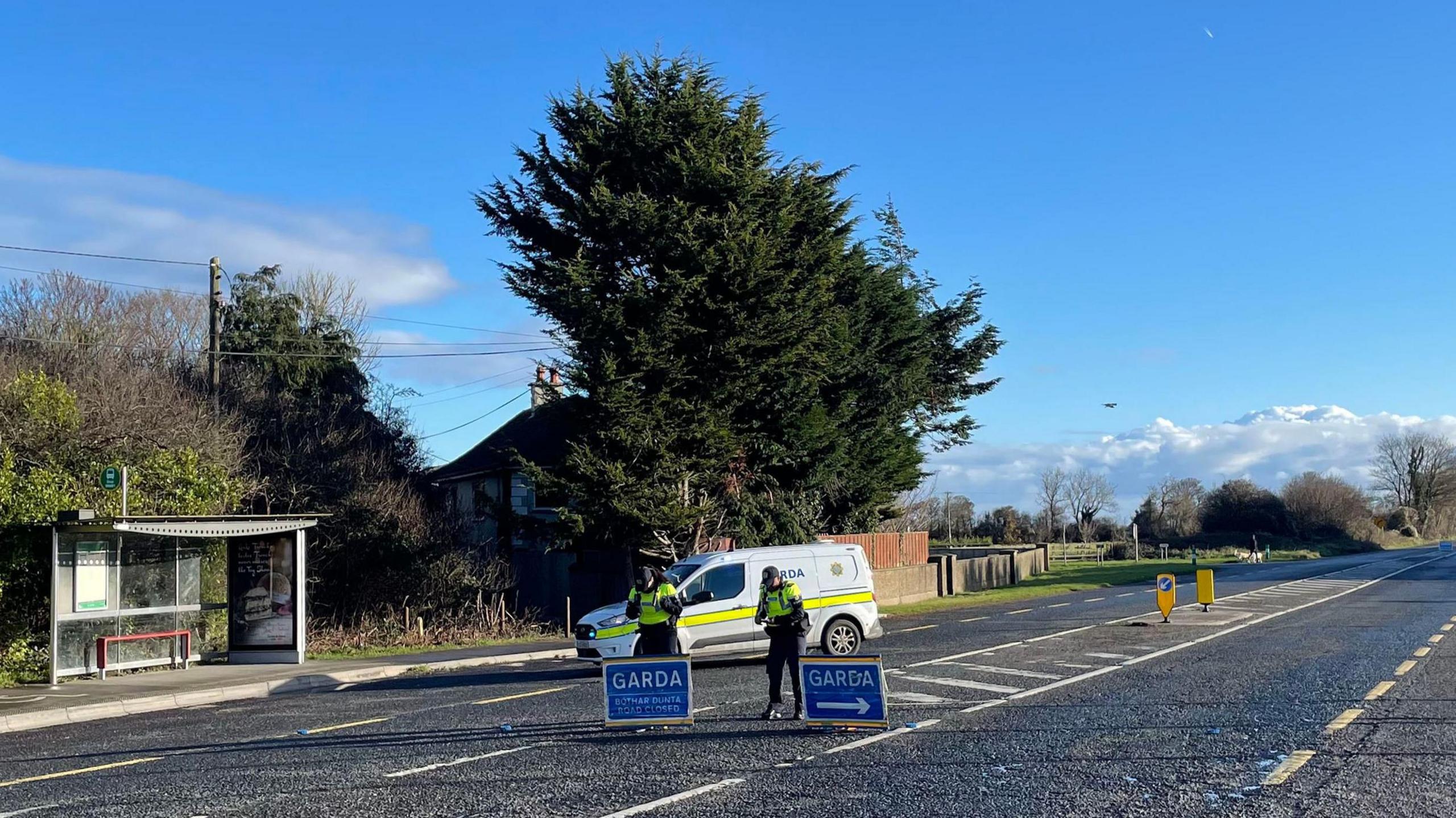 Gardaí at the scene where a road is closed near where a bus, lorry and car collided in Gormanston, Co Meath. There are two officers standing behind Garda signage. The signs are blue.