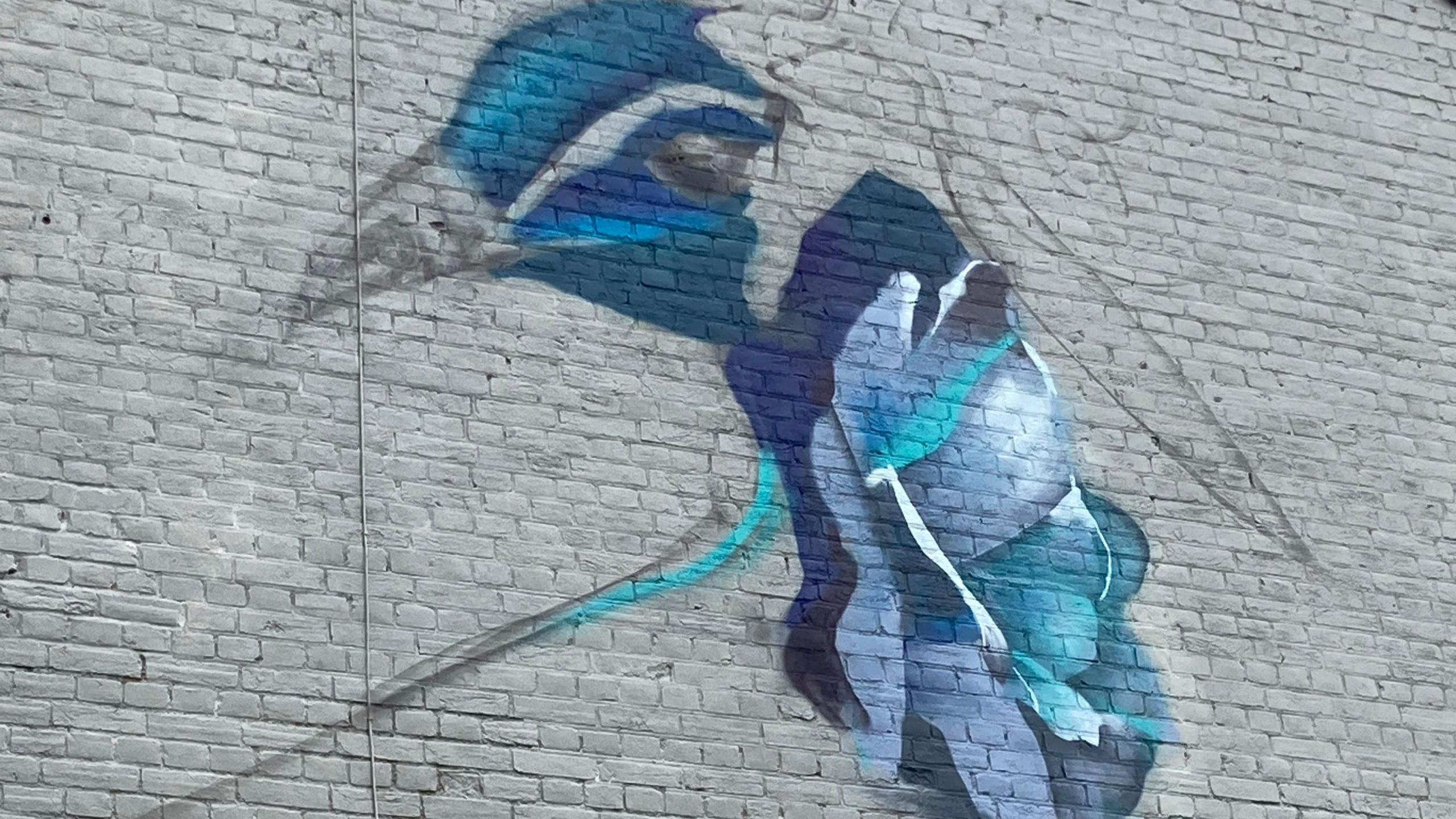 A partially finished painting of a blue and purple peacock on a grey wall.