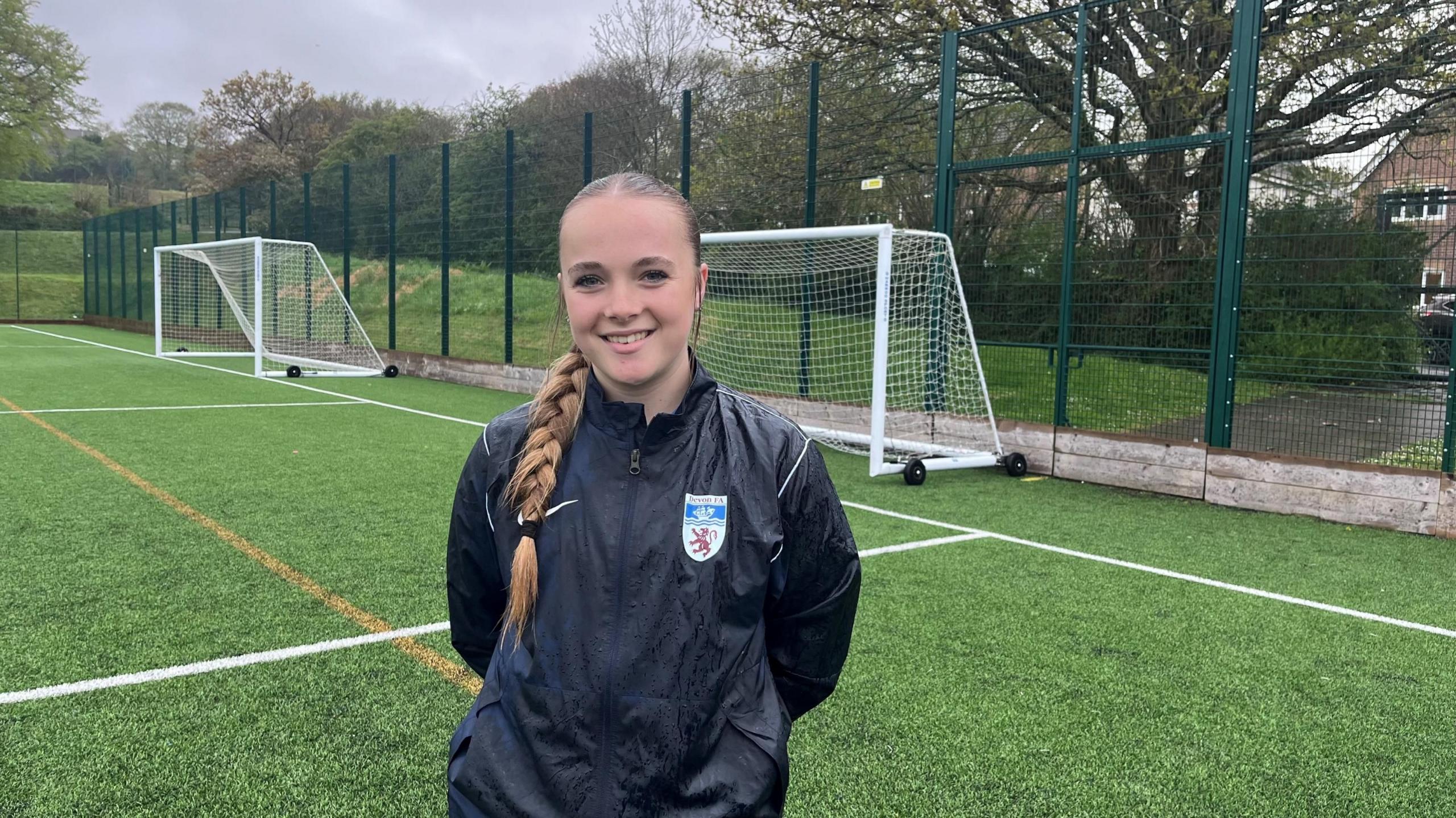 Goalkeeper Freya, 15, stands on a football training pitch in front of the goal.