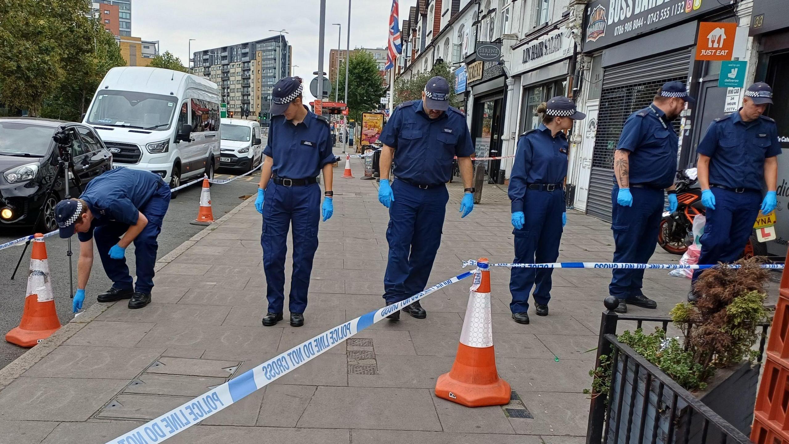 A row of six uniformed police officers search the area on Woodford Avenue in Ilford.