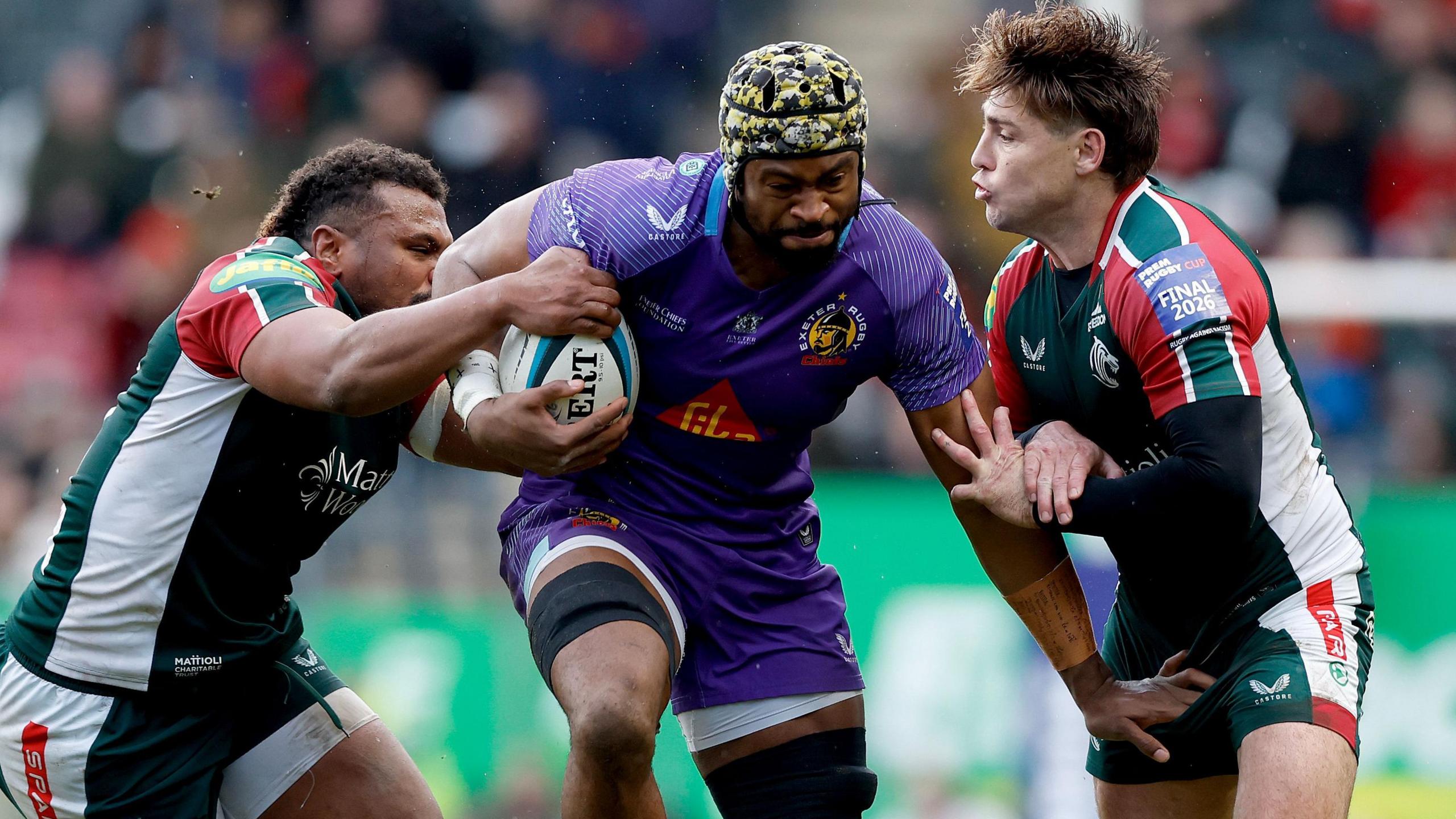 Exeter Chiefs' Christ Tshiunza bursts through the challenges of two Leicester Tigers players