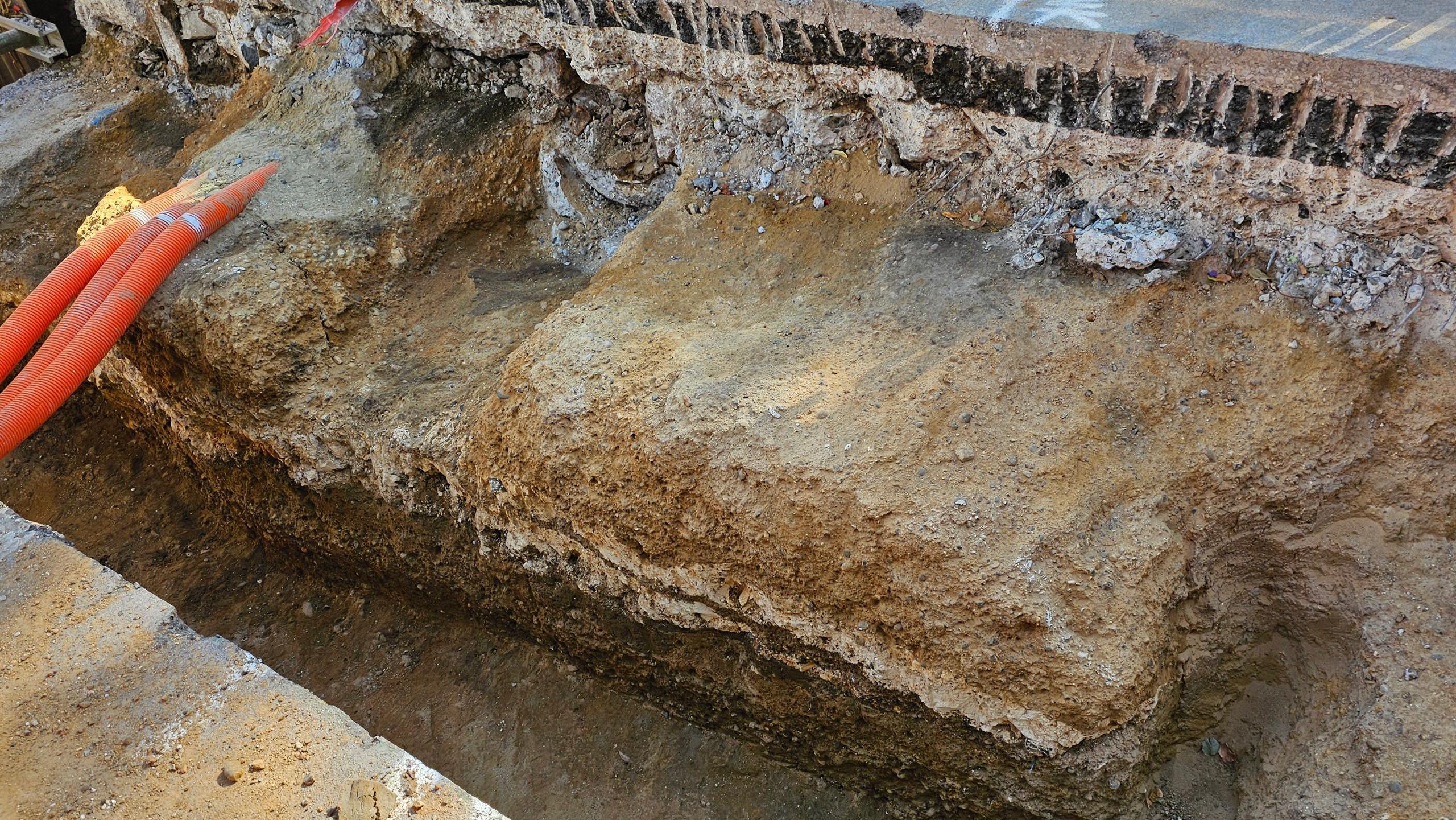 A side view showing several layers of the modern tarmac surface of Old Kent Road, with layers of roman road underneath. Orange tubes are visible to the left of the cross-section