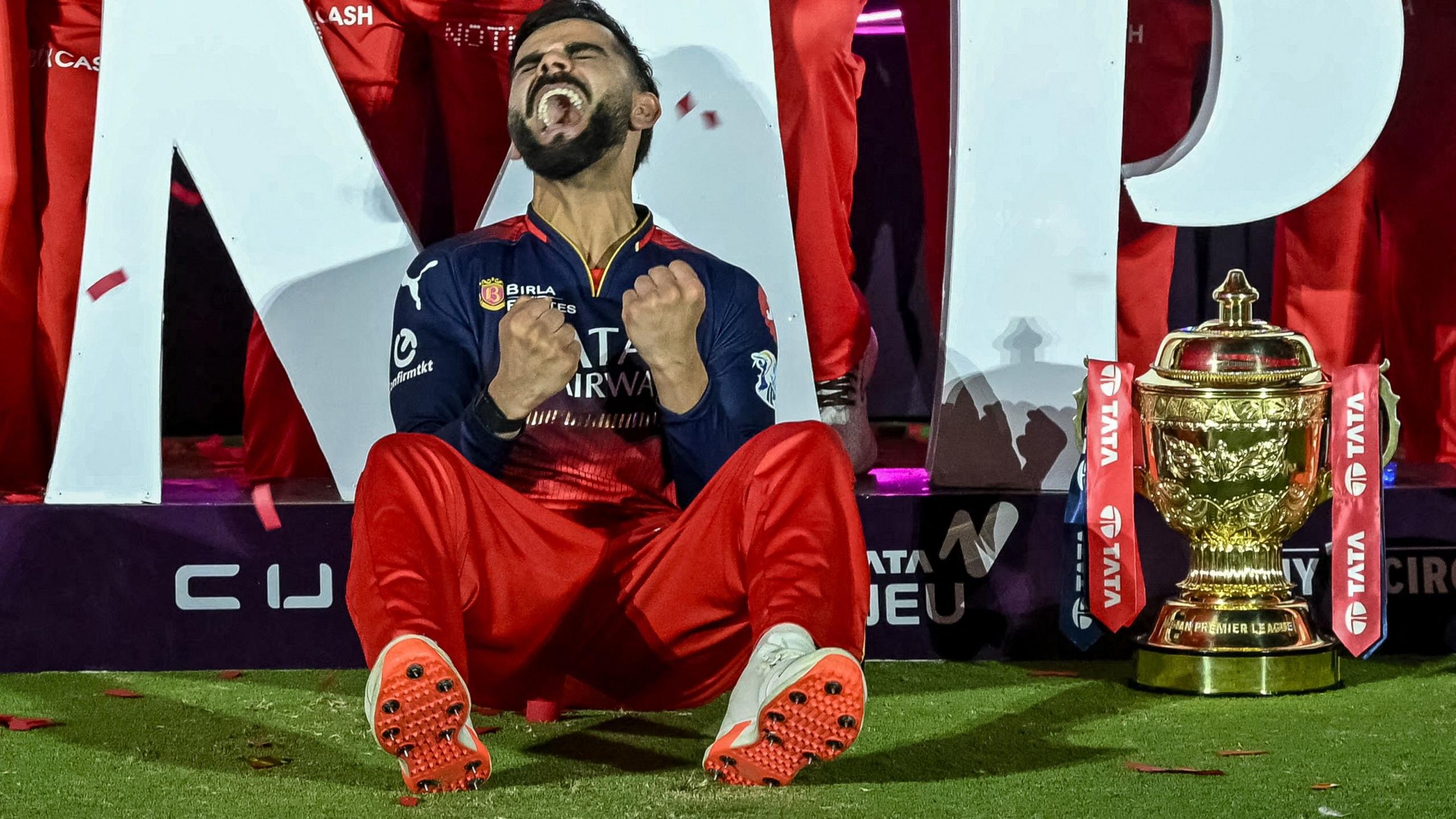 Virat Kohli cheers to himself, sat beside the IPL trophy