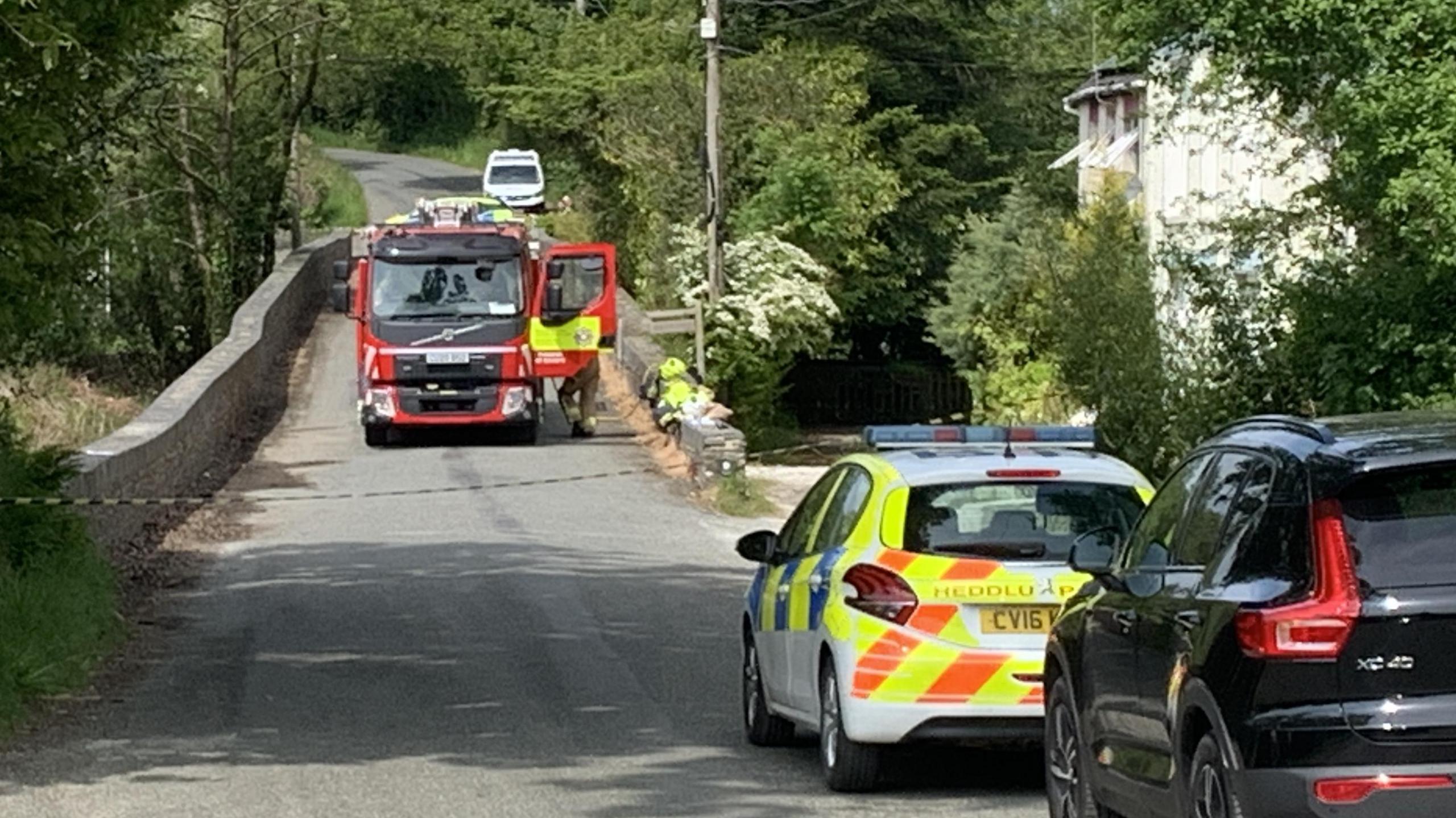 Fire engine outside a house which appears to have a burnt roof in the distance.