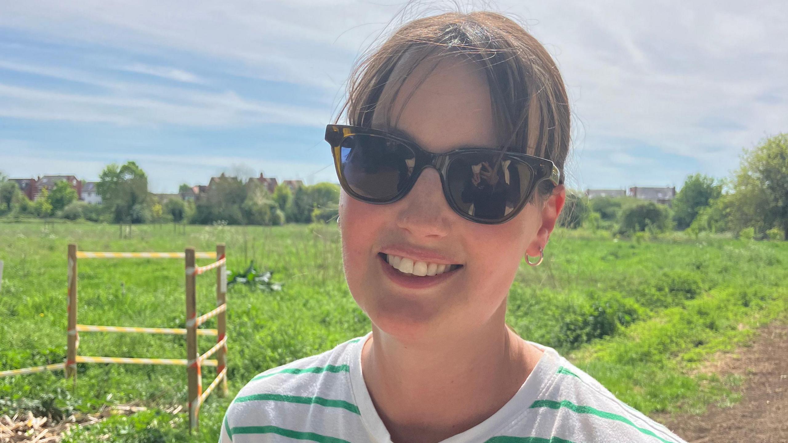 Woman wearing sunglasses and striped top on footpath.